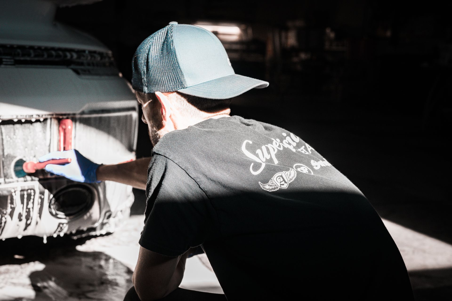 Person in a cap sprays the rear of a white truck in a garage.
