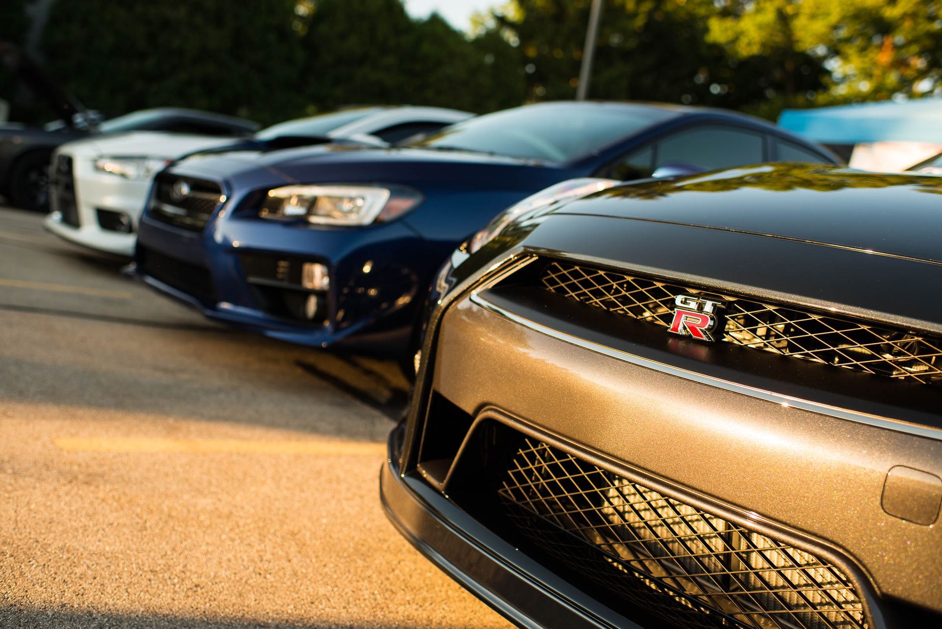 Parked sports cars, including a black Mitsubishi, lined up on a sunlit street