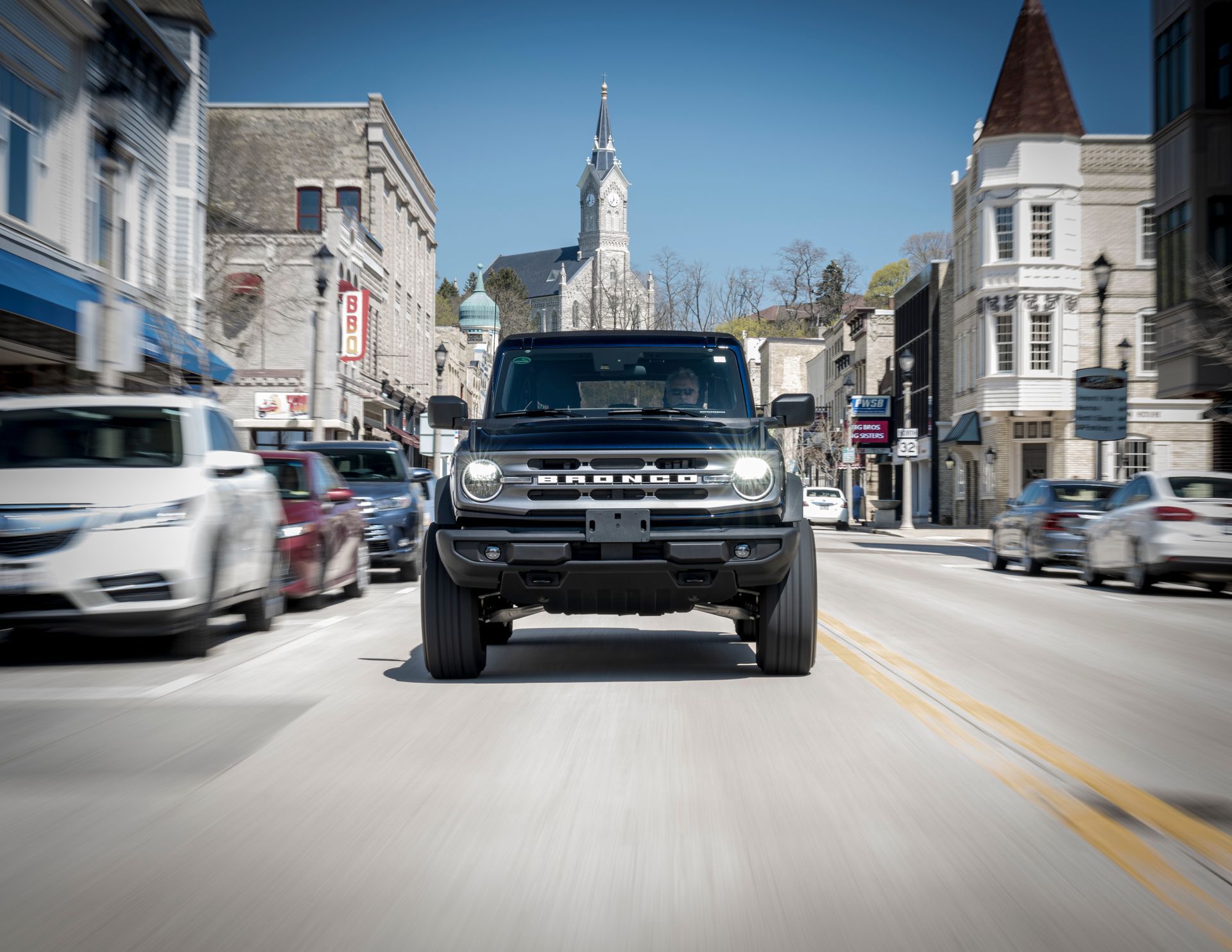 Black SUV driving down a city street with parked cars and a church in the background.