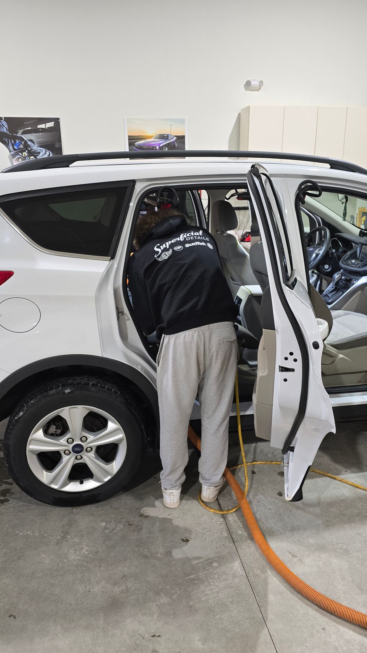 Person refueling a white SUV at a gas station, leaning into the open driver-side door.