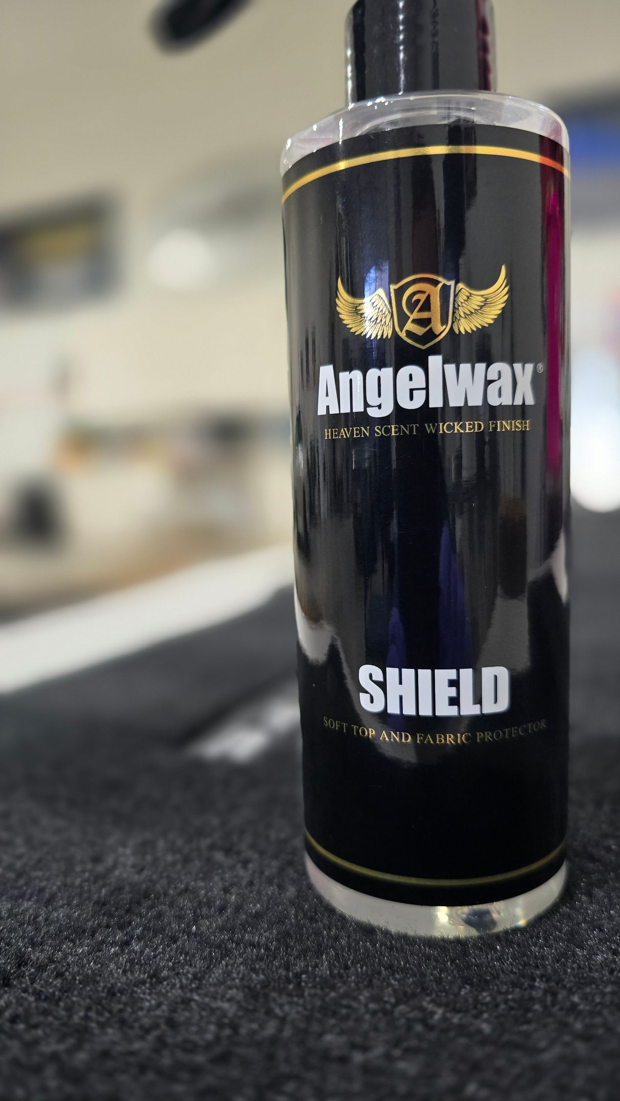 Black Yegelwax Shield bottle standing on a counter, with a blurred background.