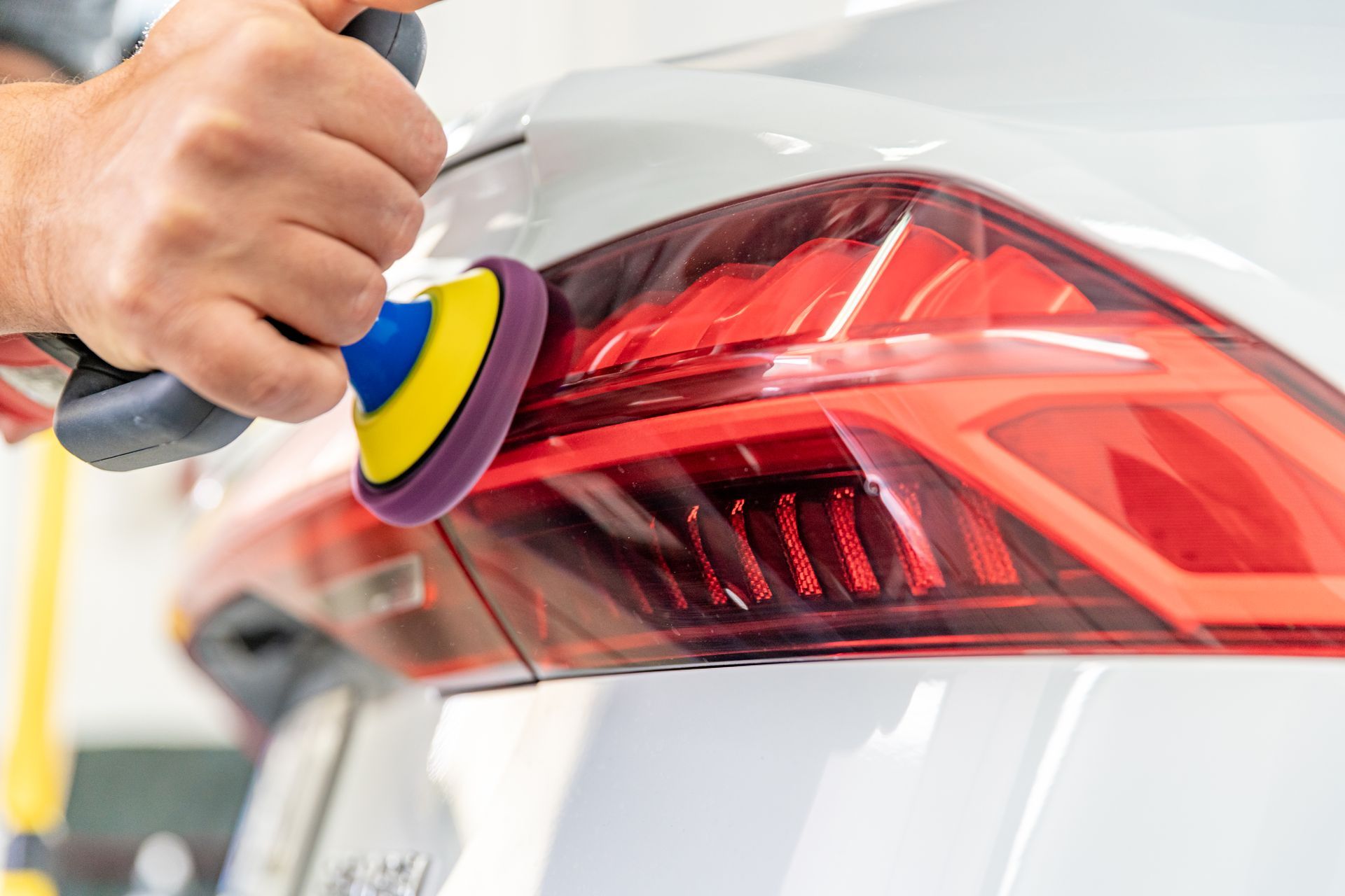 Hands polishing a white car’s red taillight with a buffer tool