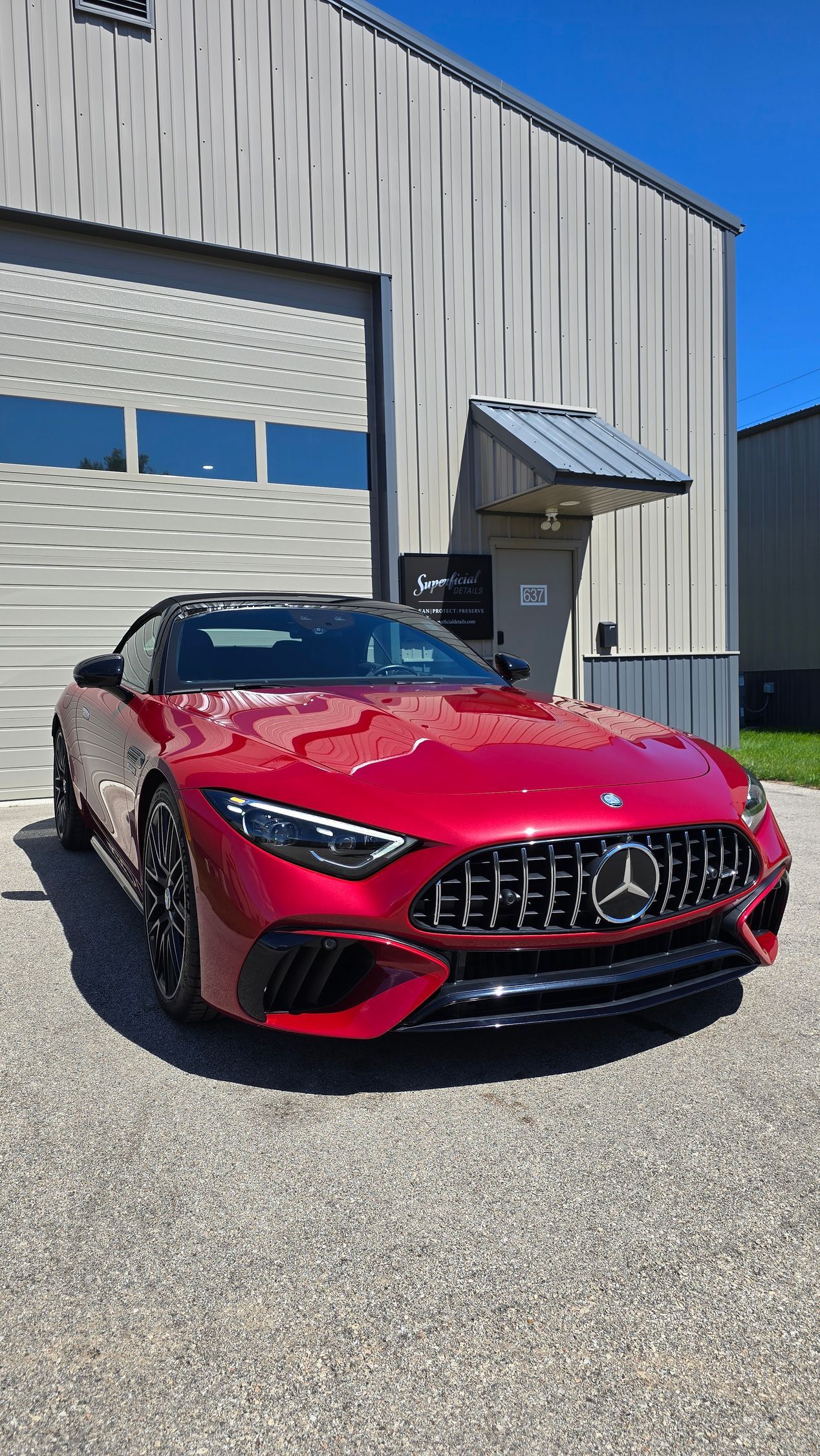 Red Mercedes sports car parked outside a metal building on a gravel lot.