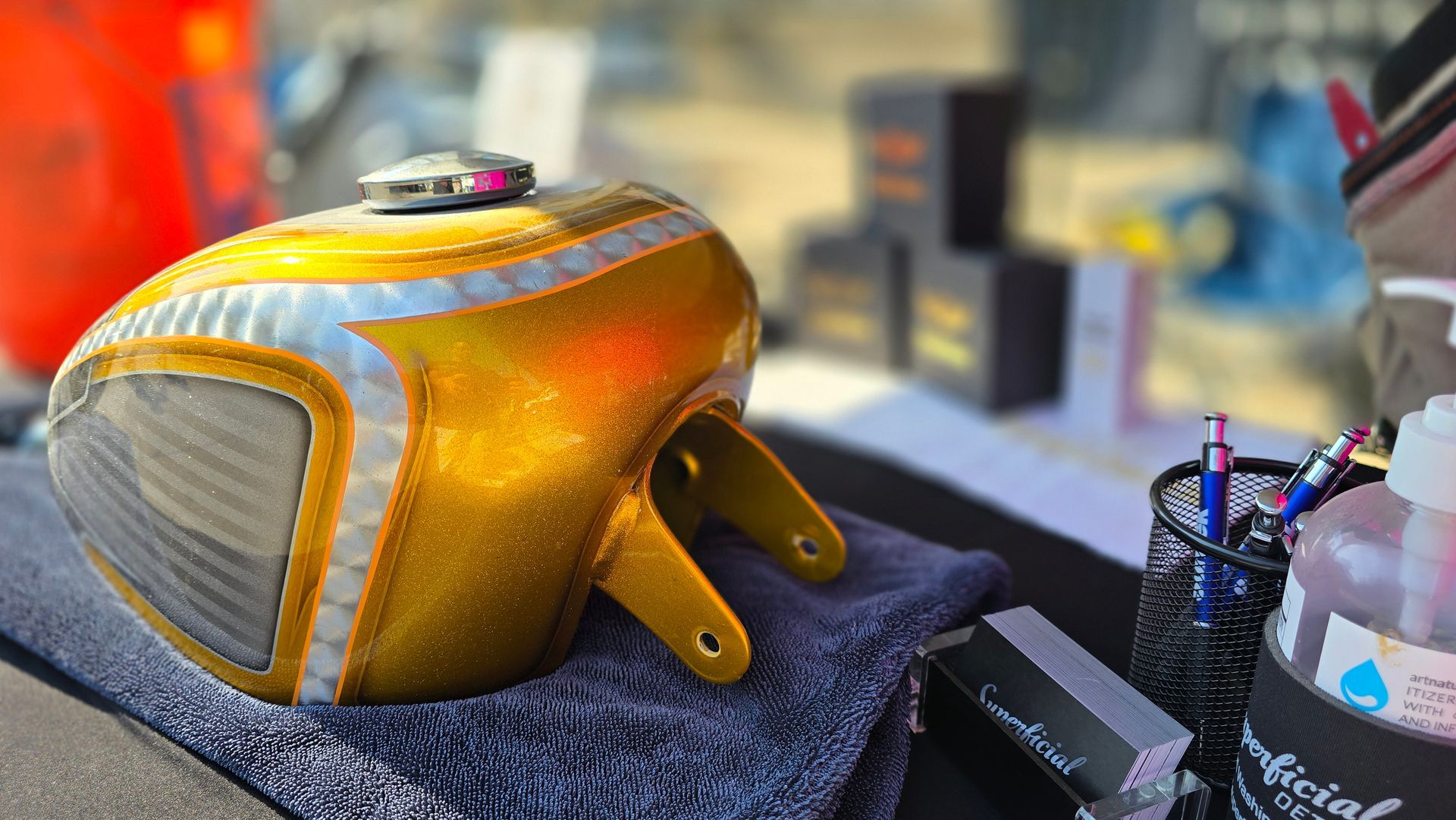 Gold motorcycle fuel tank with gray side panels resting on a dark cloth in a workshop.