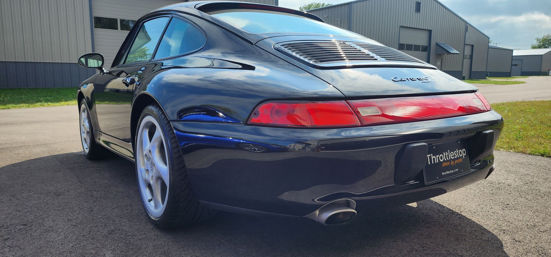 Black Porsche sports car parked on pavement outside a large industrial building