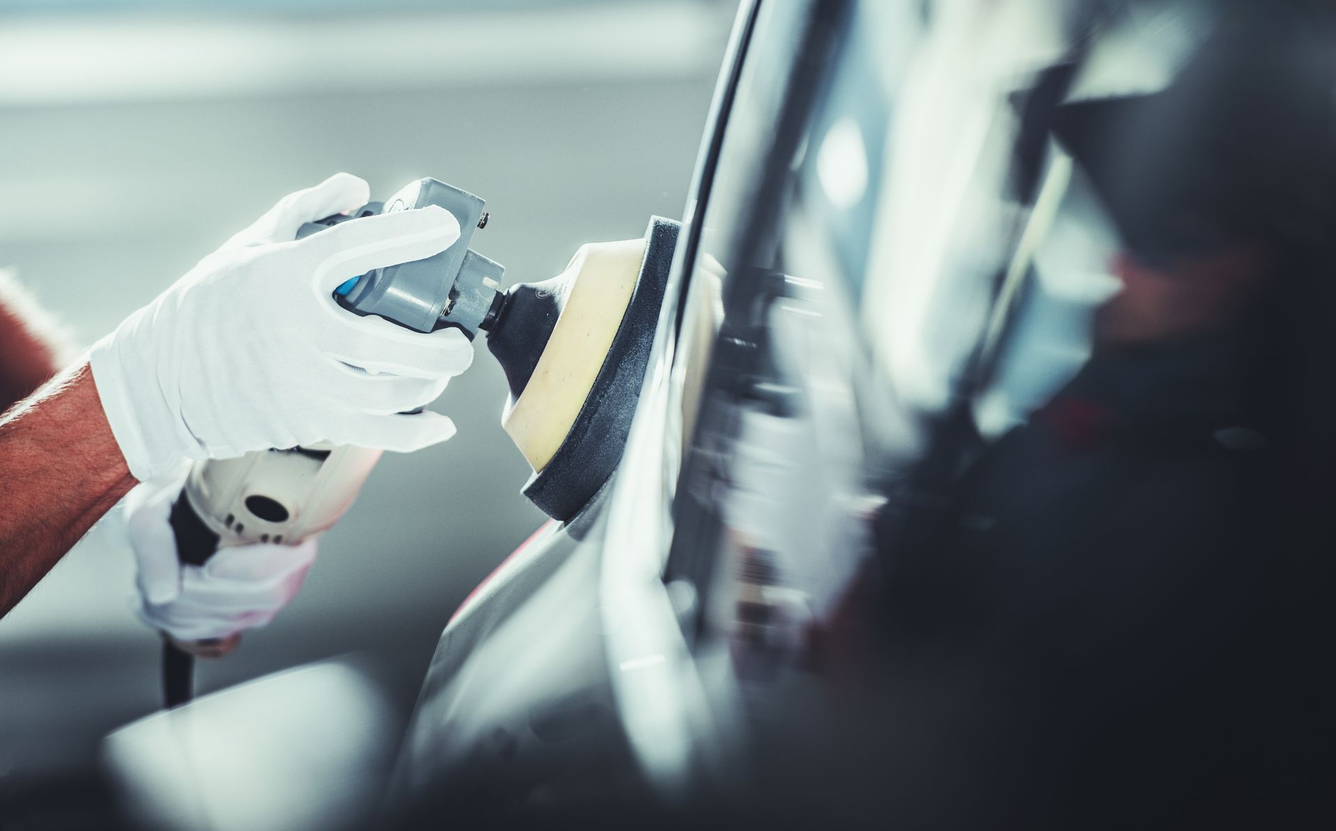 Gloved hands polishing a car’s side panel with a buffer