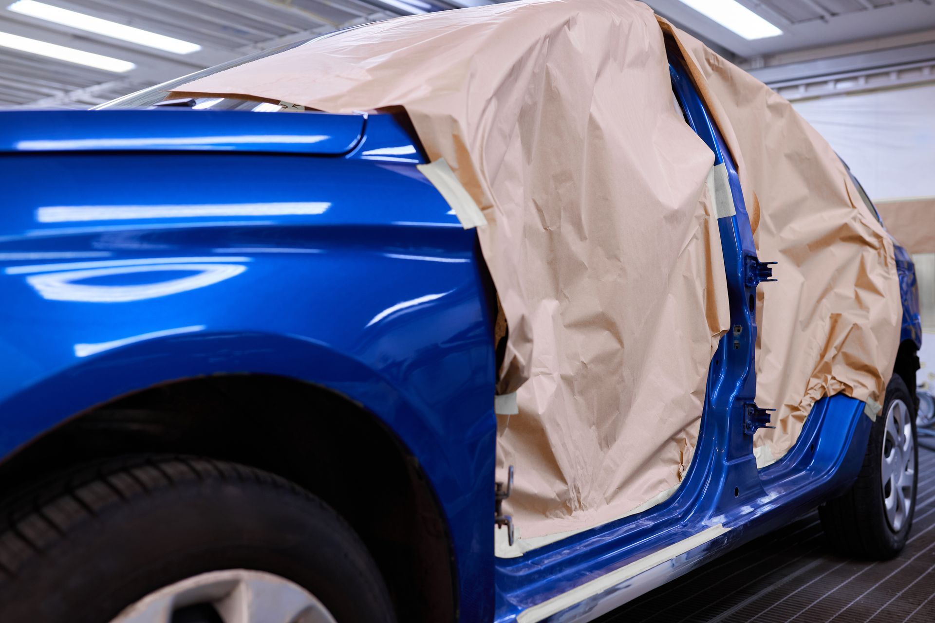 Blue car covered with masking paper in a paint shop, mid-repair