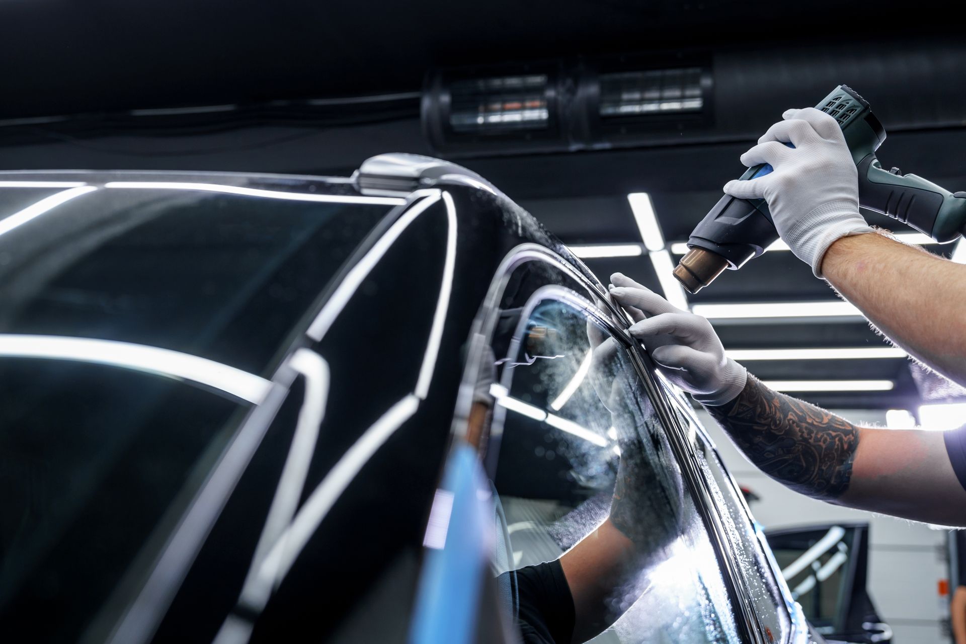 Technician polishing a black car in a bright auto detailing shop