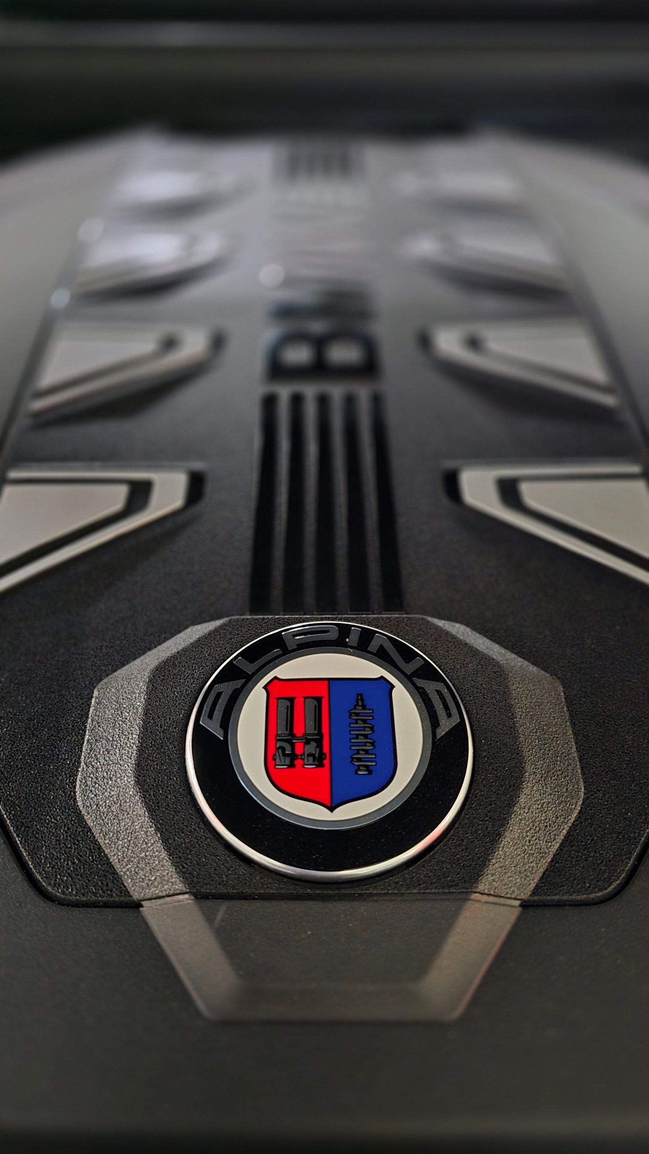 Close-up of a black car hood badge with red and blue emblem on a textured surface