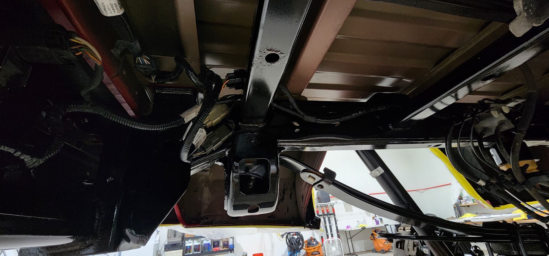 Underside of a vehicle on a lift in a garage, showing suspension, exhaust, and undercarriage parts