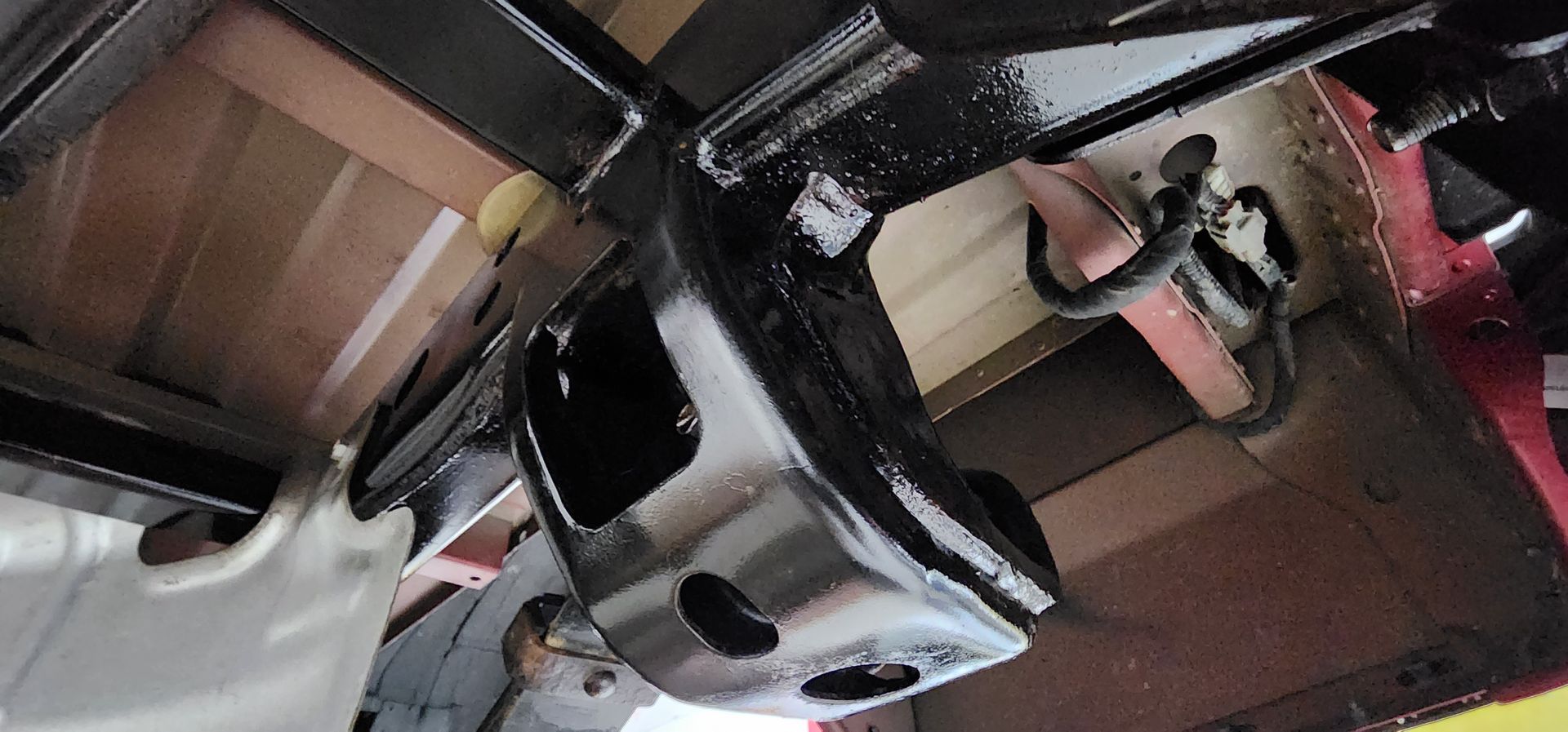 Close-up of a black car bumper and chrome wheel in a garage or workshop at an angle