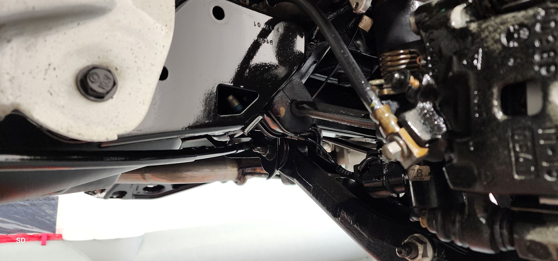 Close-up of a motorcycle underside, showing black frame, suspension, and engine components.