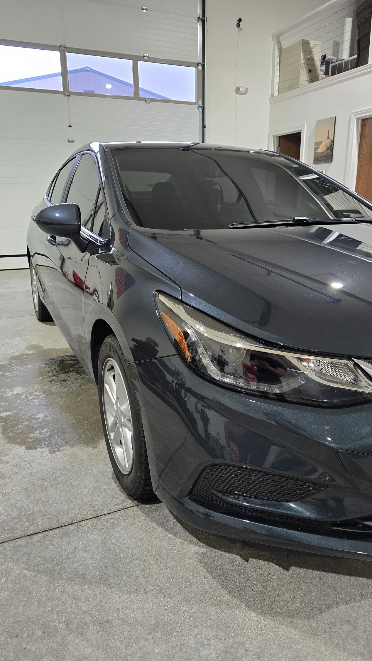 Dark gray sedan parked inside a garage with a concrete floor and large door windows