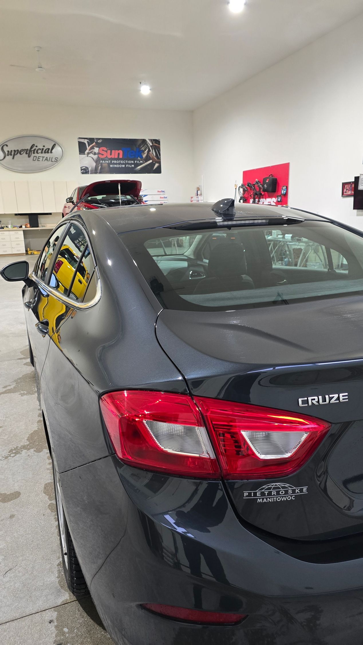 Black sedan parked in a garage, rear view with red taillights and white wall-mounted signs.
