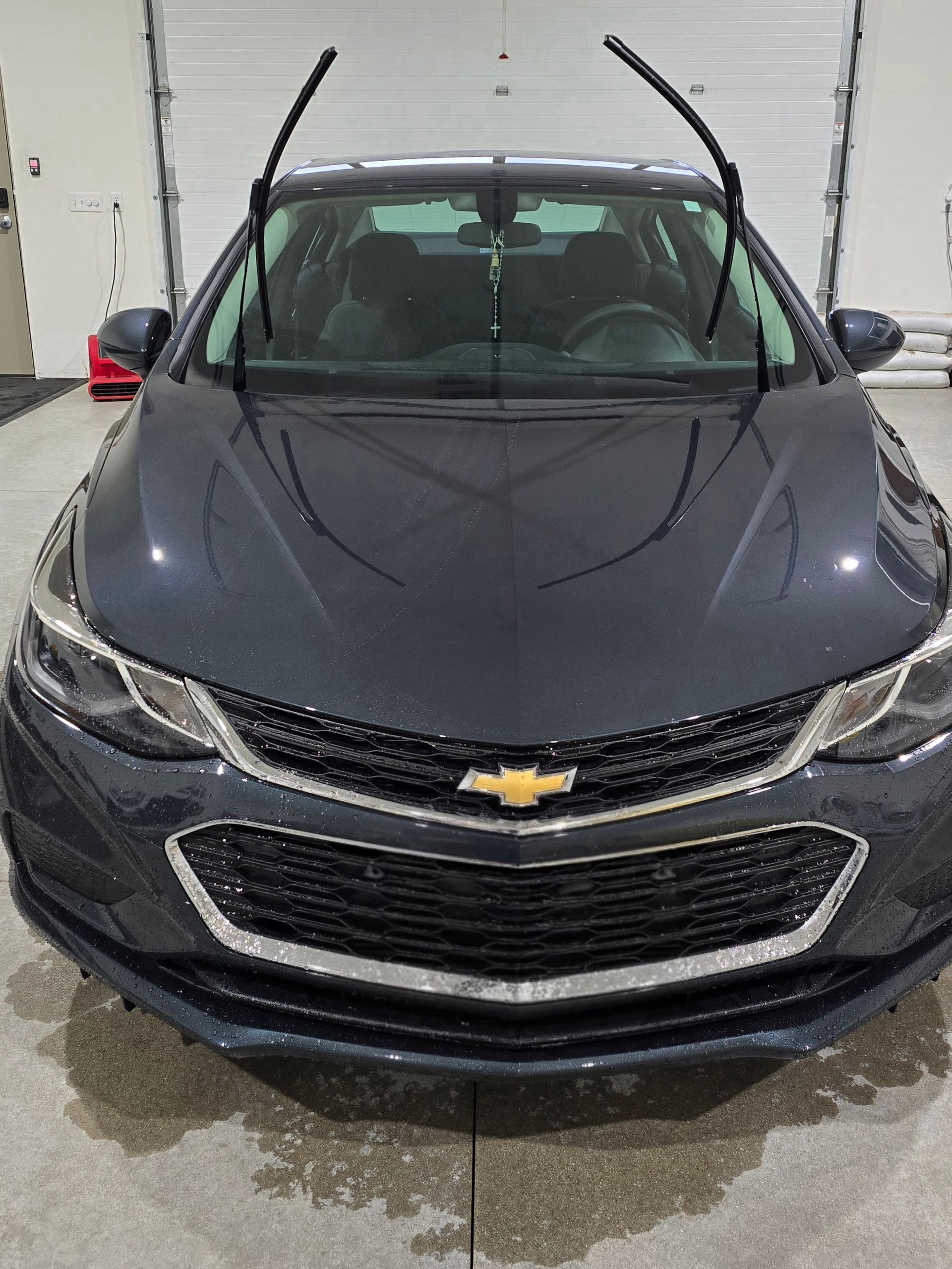 Front view of a gray Chevrolet sedan with windshield wipers raised in a garage.
