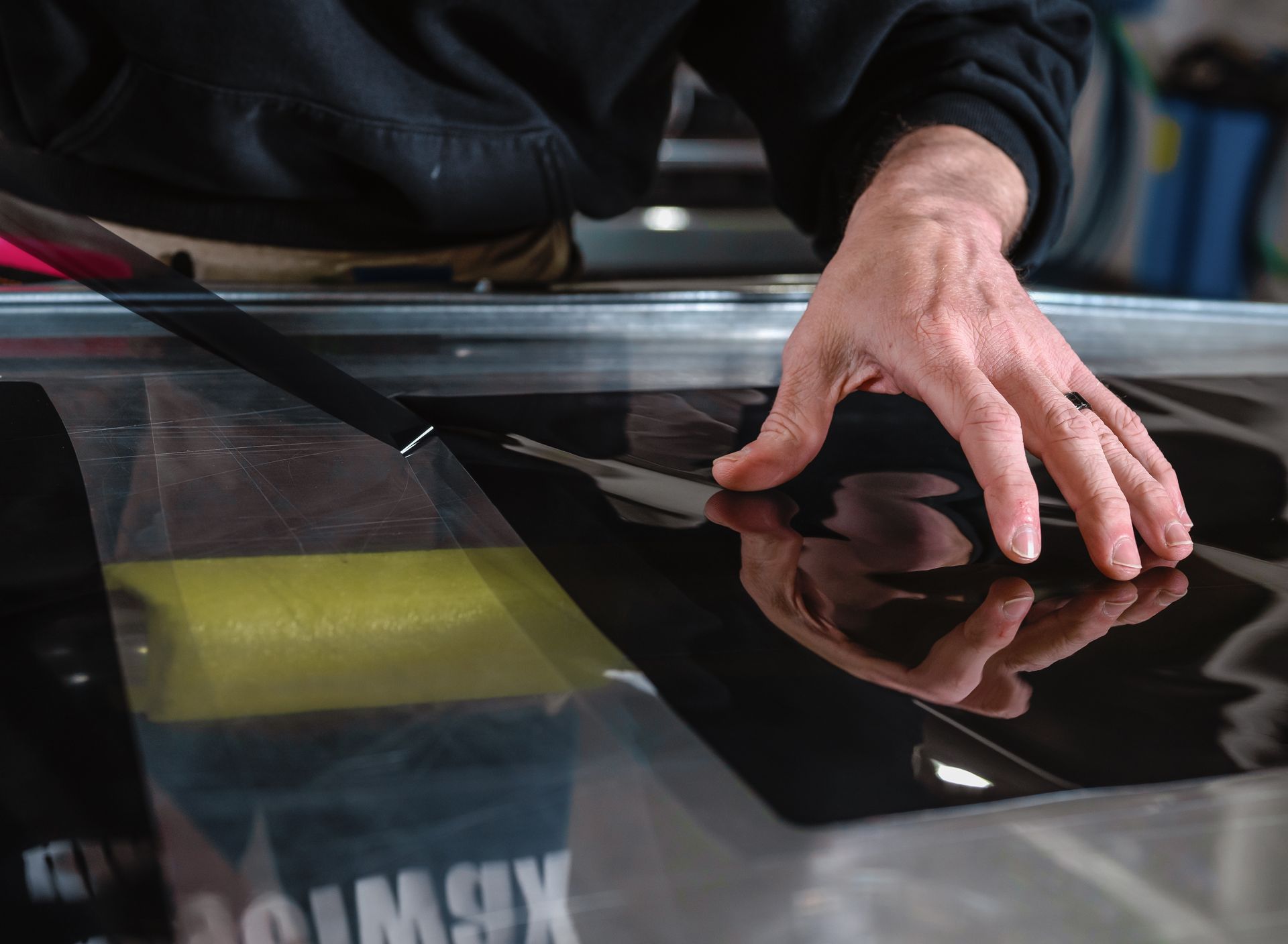 Hands smoothing black vinyl on a print shop machine, with a reflective surface visible.