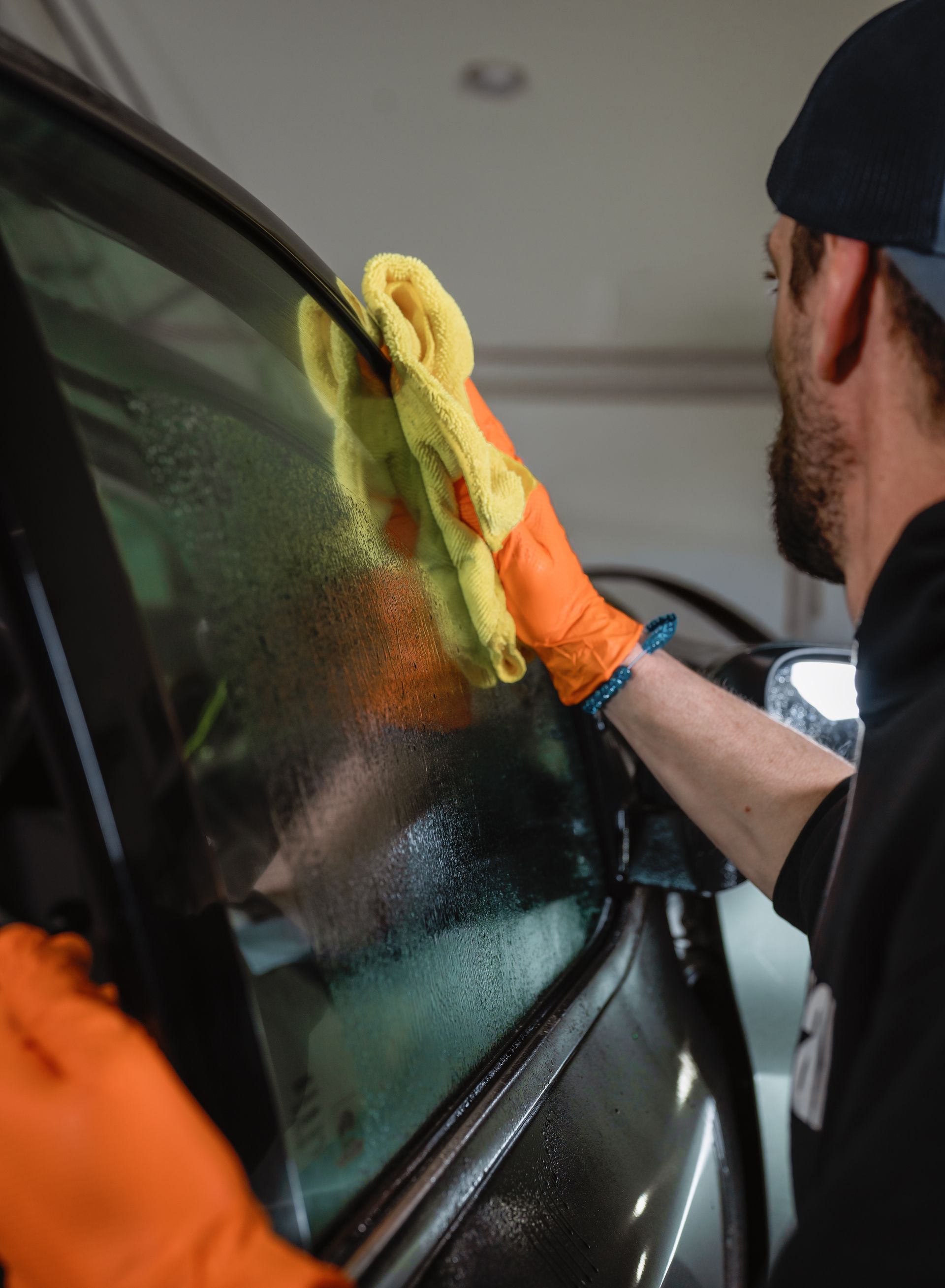 Person cleaning a car window with a yellow cloth and orange gloves