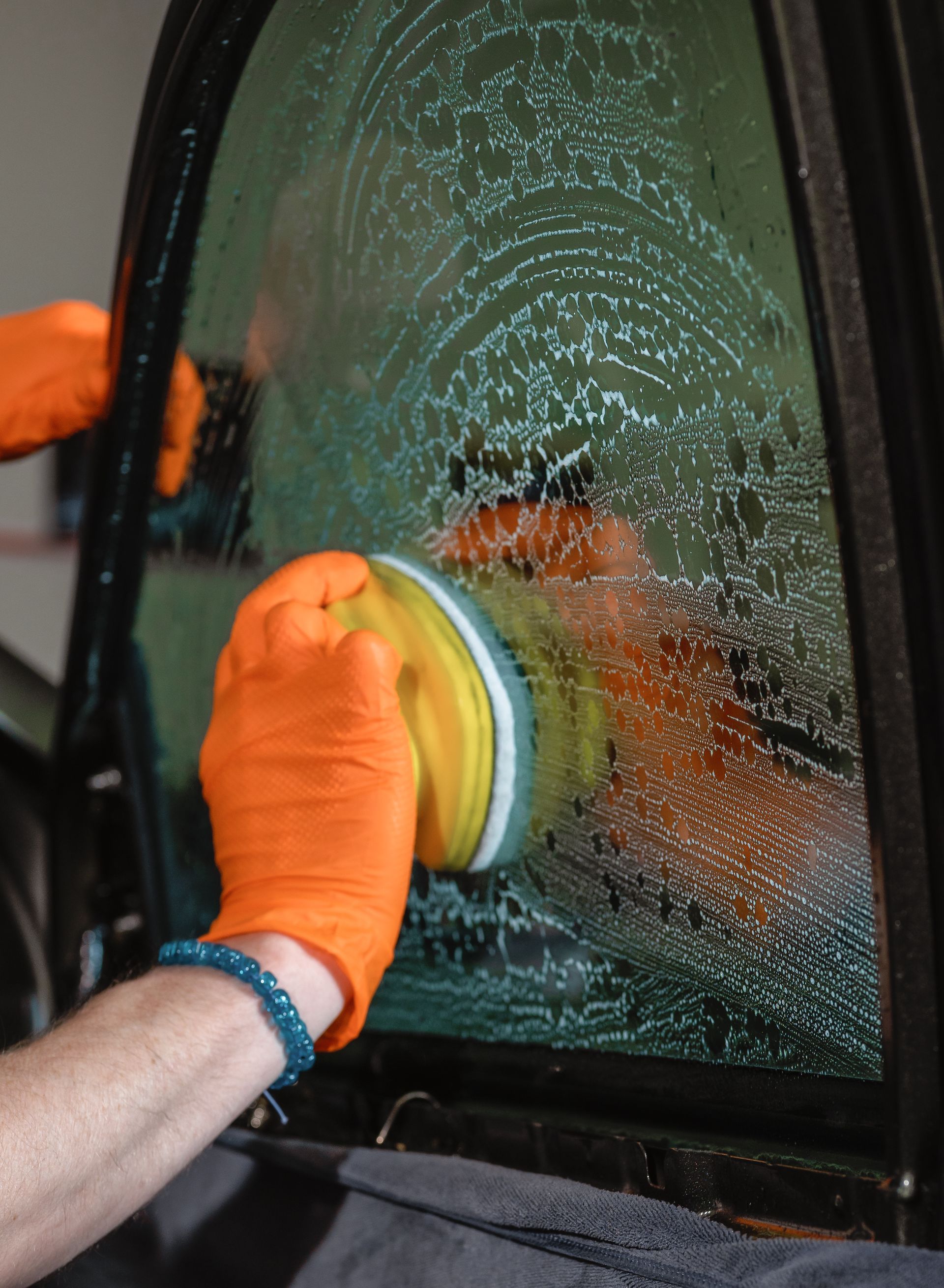 Gloved hands scrubbing a car window with a sponge and soapy water