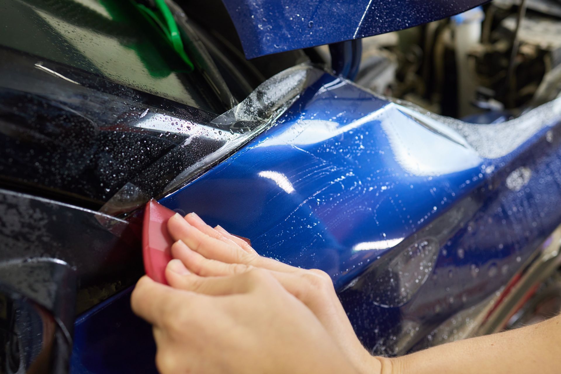 Hands sanding or polishing a blue motorcycle fairing with a pink pad