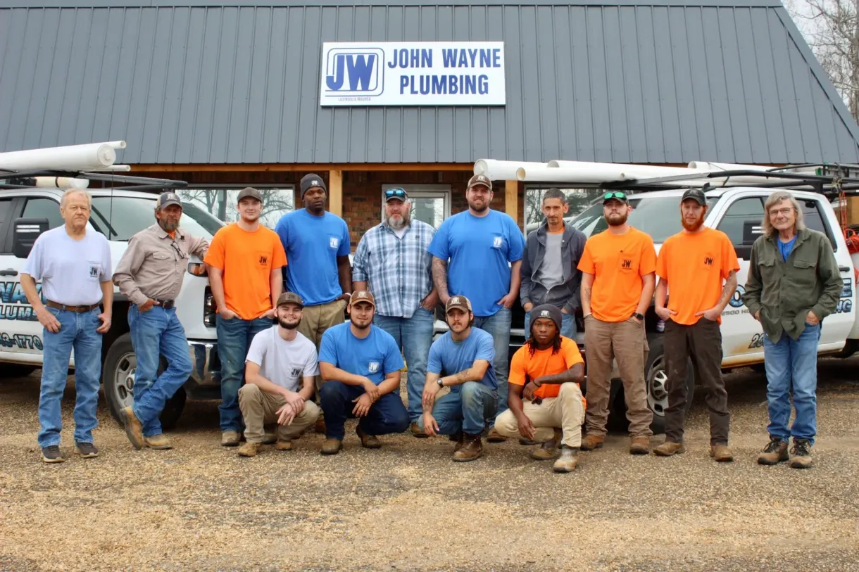 Group of plumbing workers posing in front of a John Wayne Plumbing building.