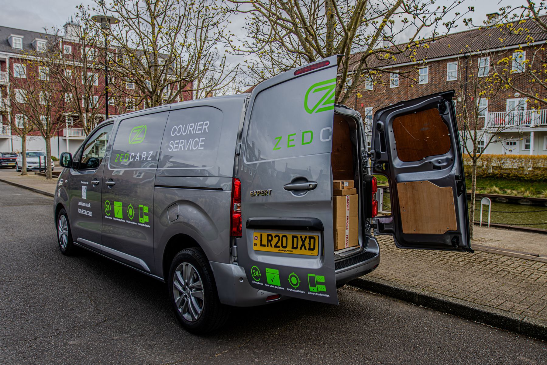Gray delivery van with rear door open, parked on a street with buildings in the background