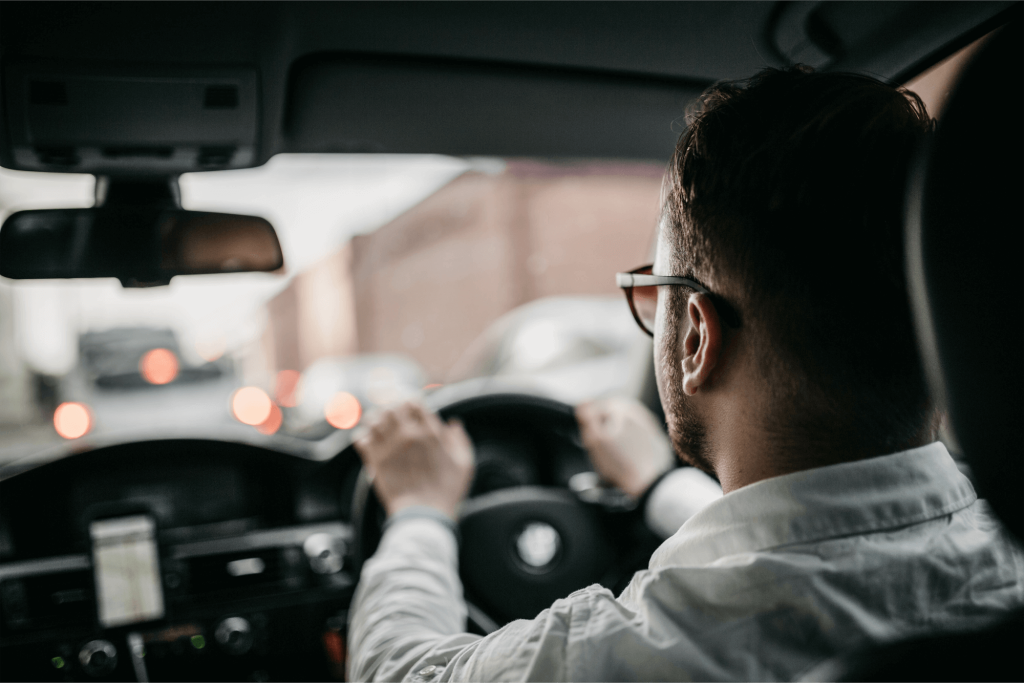 Driver viewed from behind at the wheel in a car, looking out at traffic with blurred city lights ahead