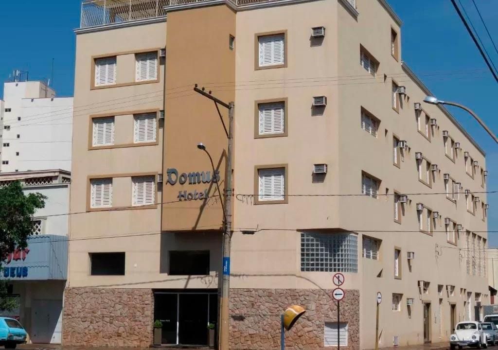 Um edifício de vários andares do Hotel Domus com paredes de estuque bege, um detalhe central marrom e um térreo com textura de pedra.