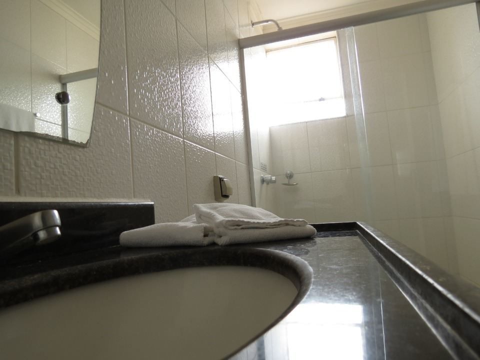 Uma pia de banheiro com bancada escura e uma pilha de toalhas brancas dobradas em frente a um box de vidro.