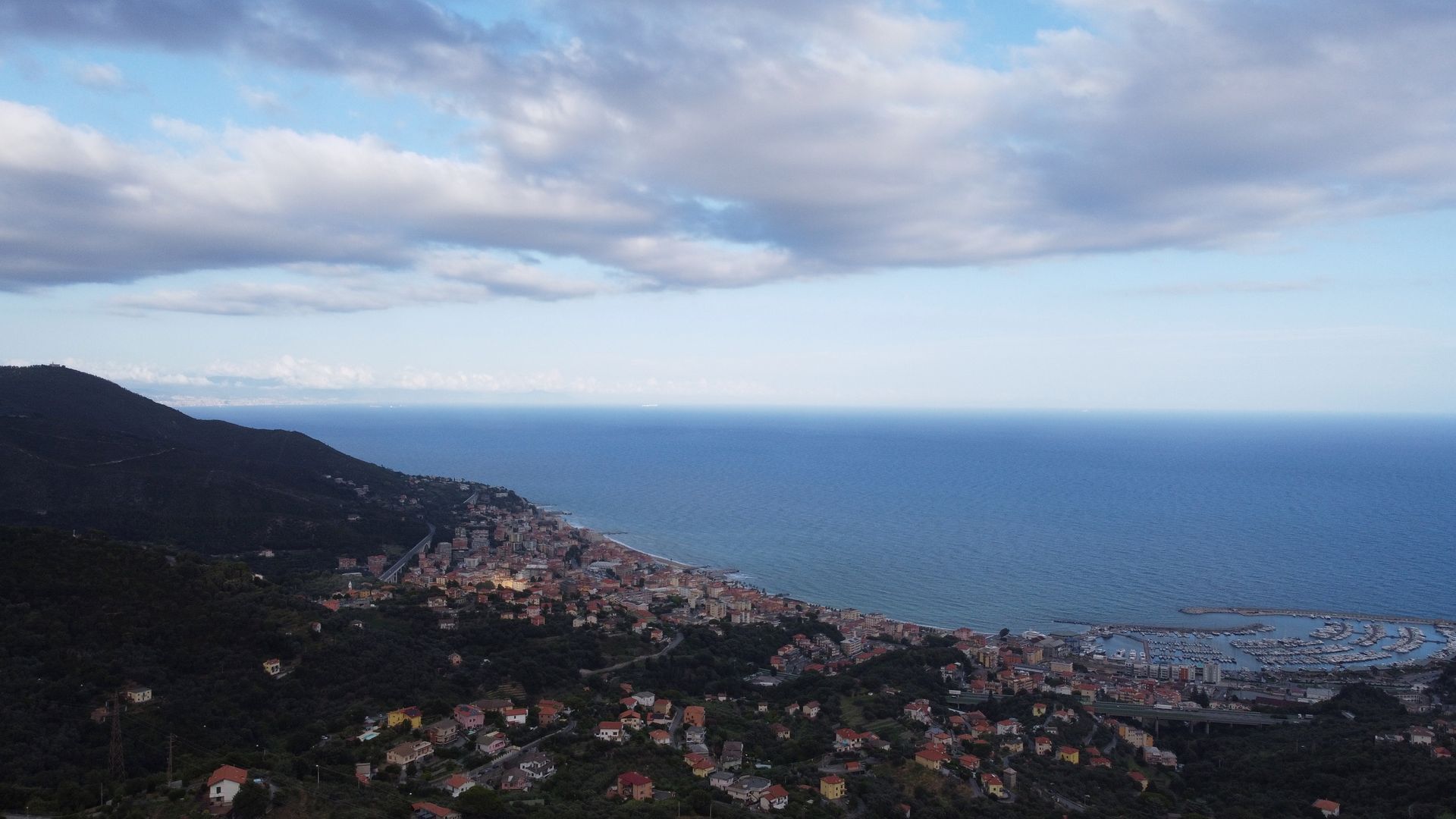 Città costiera incastonata tra le montagne e il mare, sotto un cielo parzialmente nuvoloso.