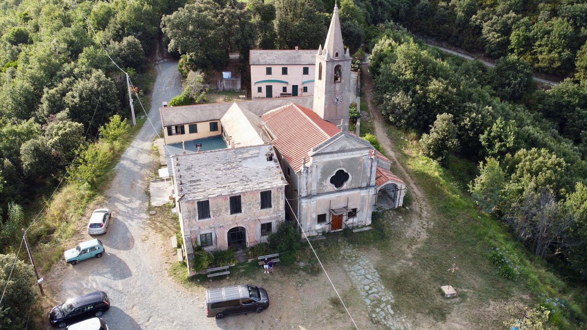 Vista aerea di un complesso di chiese con un alto campanile, circondato da alberi e un parcheggio per auto.