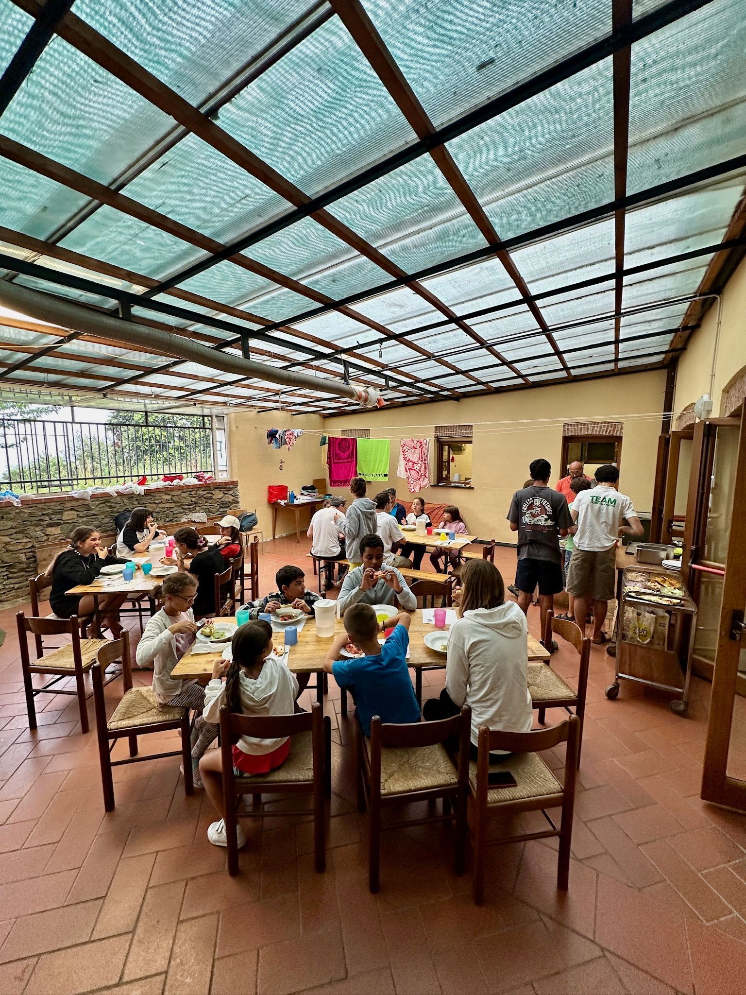 Persone che mangiano seduti ai tavoli in una zona pranzo esterna coperta.