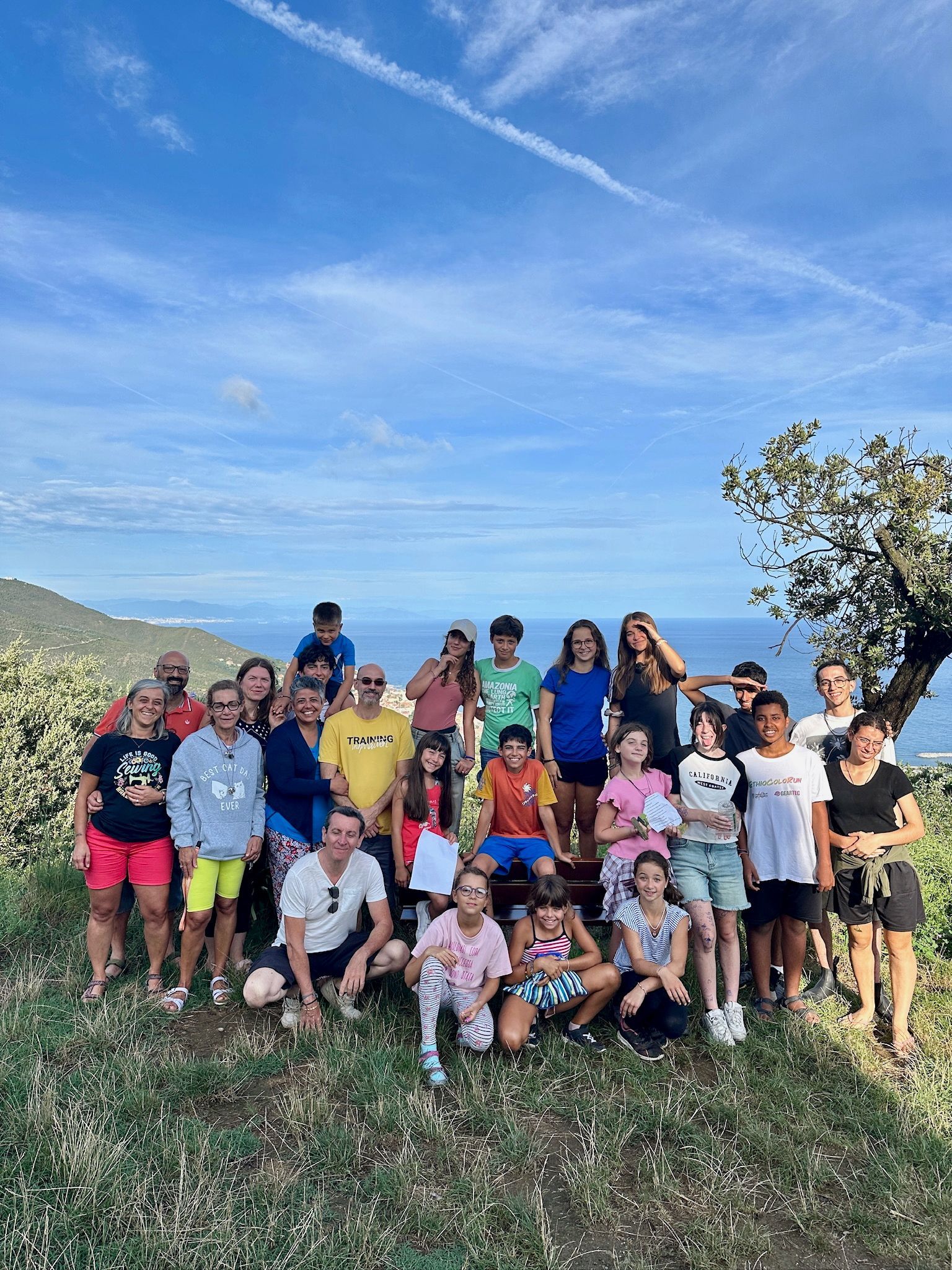 Gruppo di persone in posa all'aperto con vista sull'oceano. Giornata di sole, alcuni sorridenti.