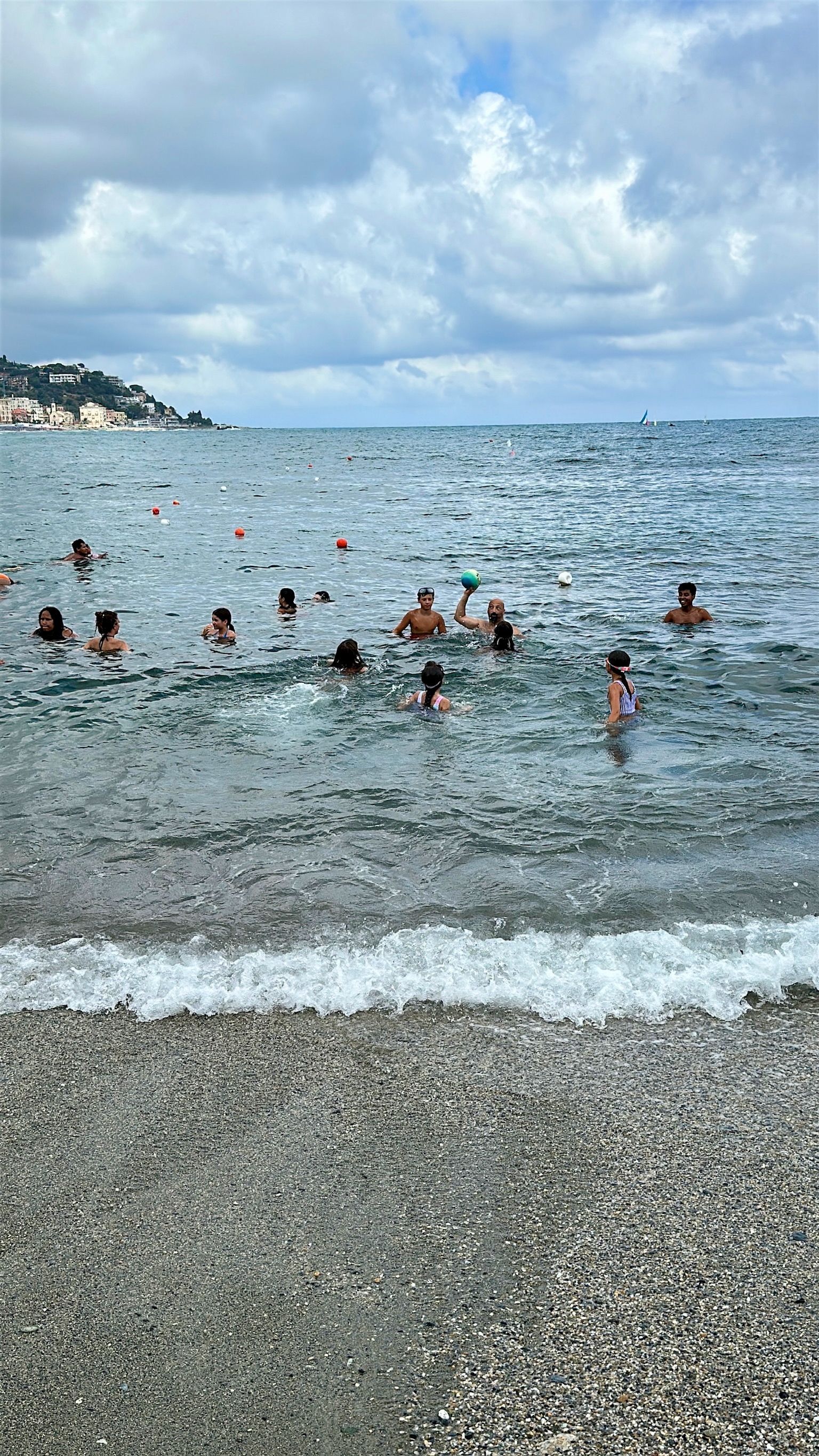 Le persone nuotano in un oceano agitato in una giornata nuvolosa su una spiaggia di ciottoli.
