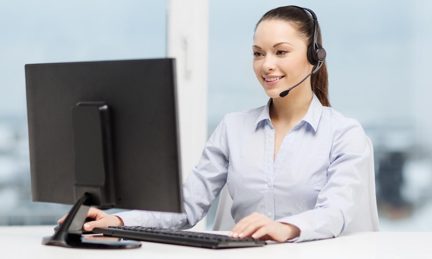 A woman wearing a headset is sitting in front of a computer.