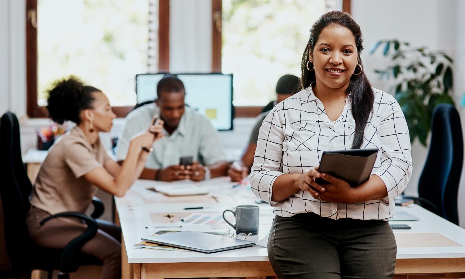 A woman is sitting at a desk in an office holding a tablet.