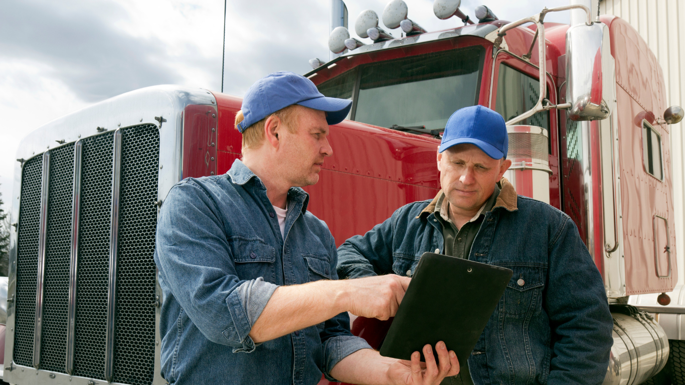 Two men are looking at a clipboard in front of a semi truck.