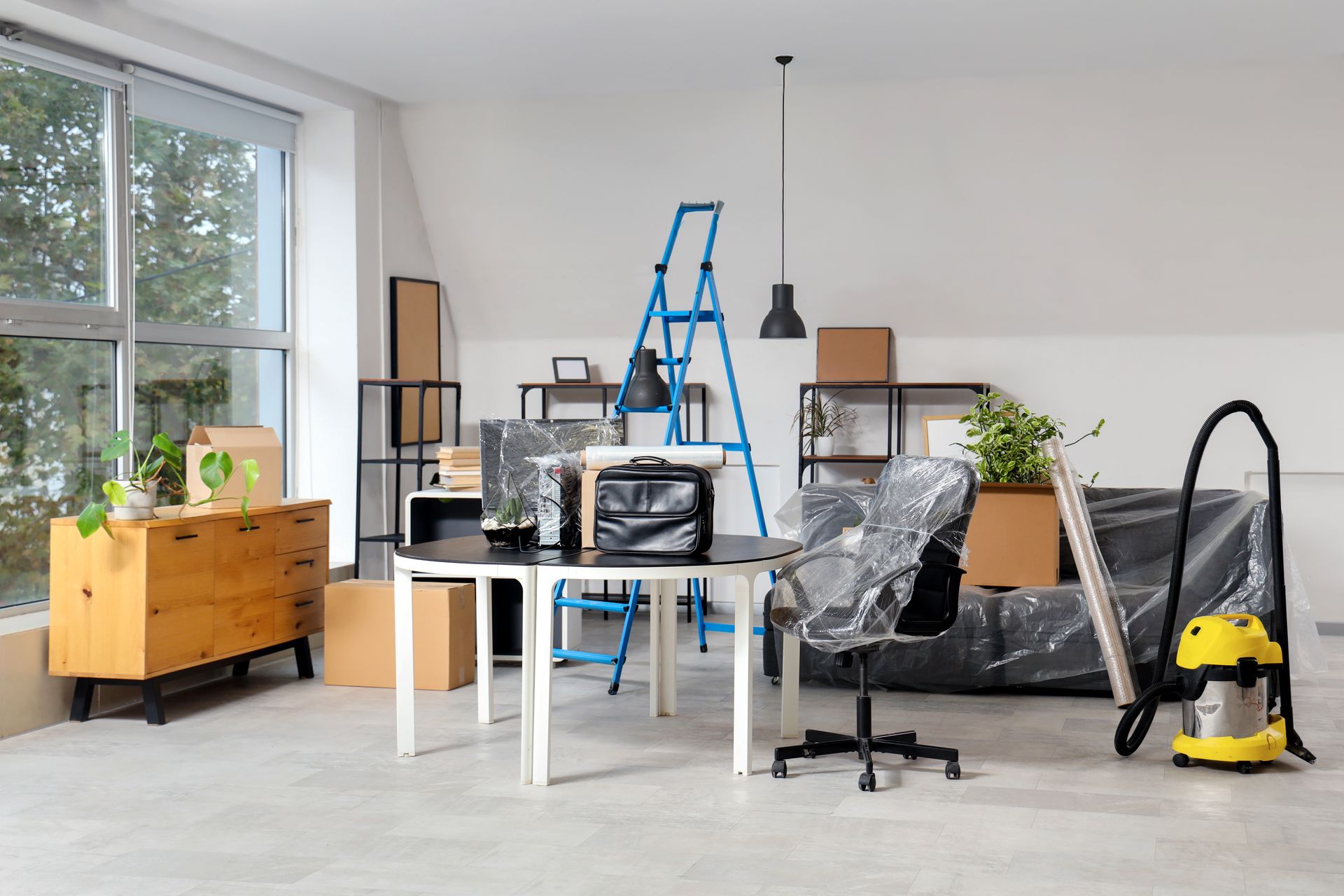 Messy living room with ladder, boxes, furniture, and a vacuum during home renovation