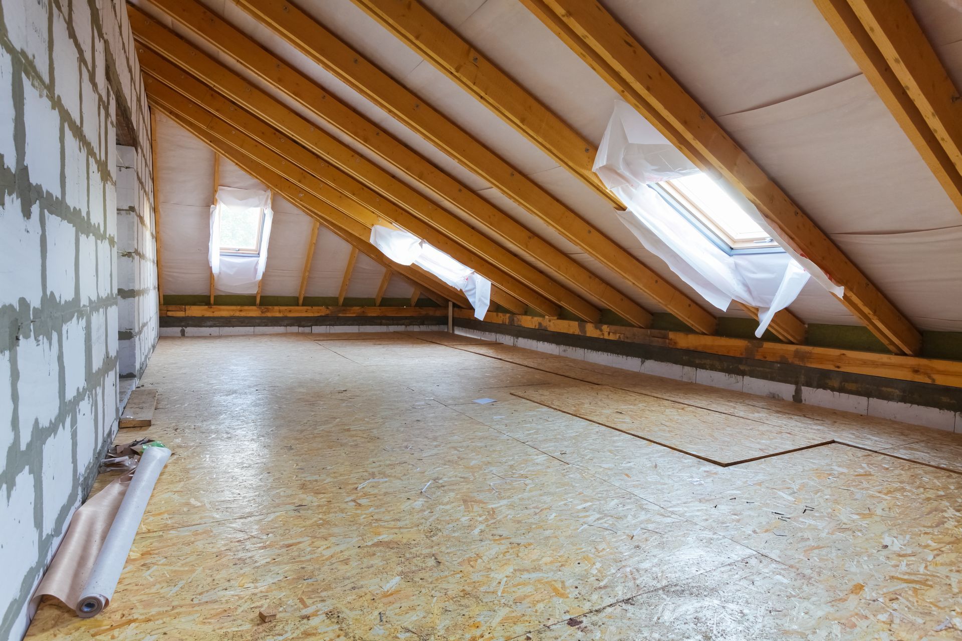 Empty attic with slanted wooden beams, skylights, and unfinished floorboards.