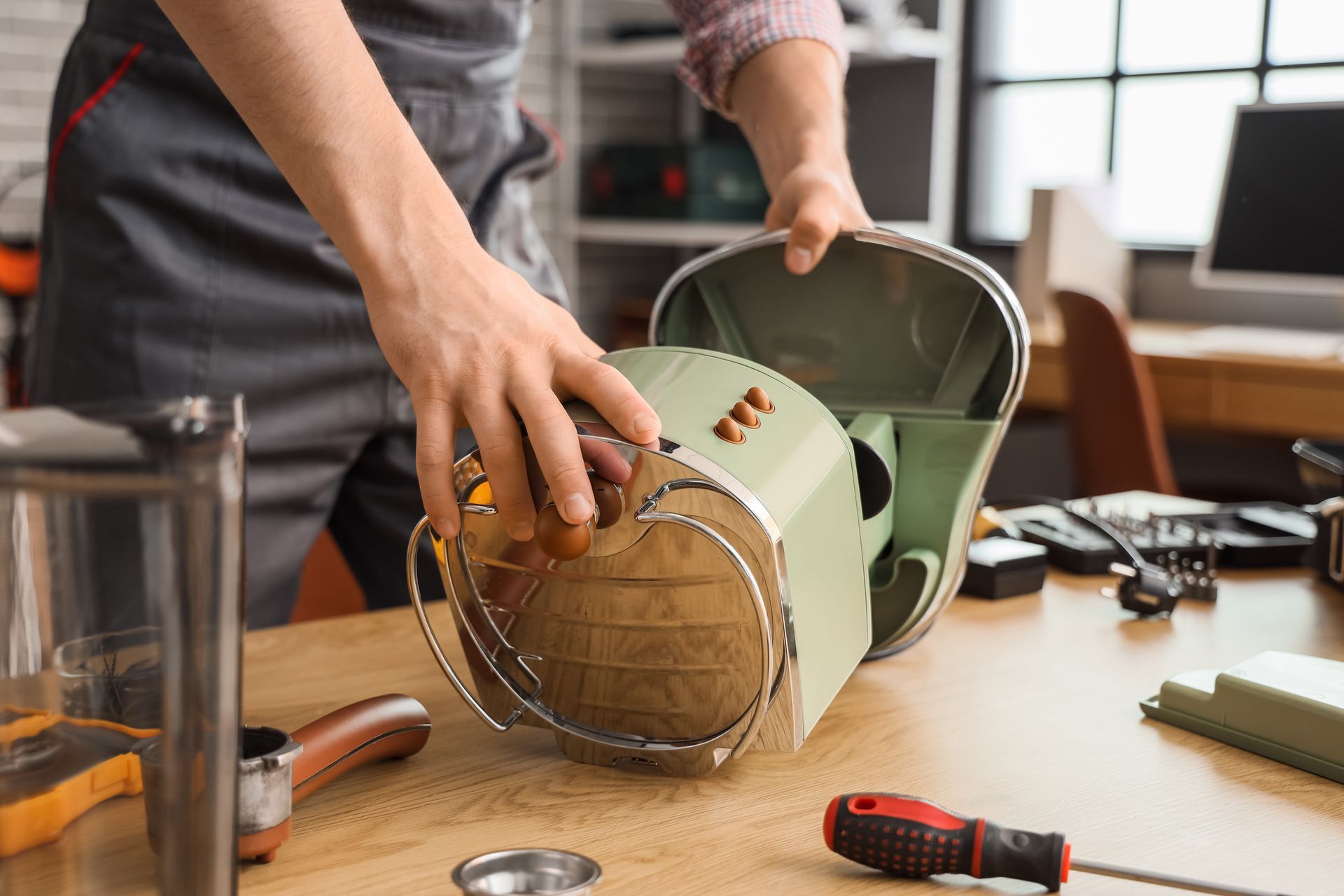 Hands assembling a green countertop appliance on a wooden table with tools nearby