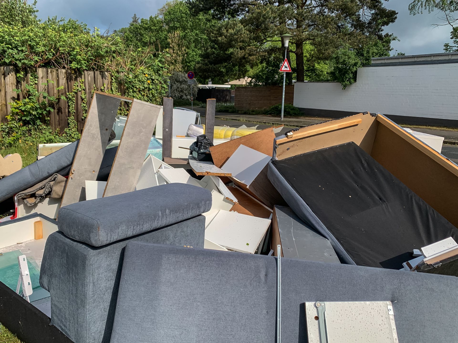 Piled debris and discarded furniture in a backyard near a fence and trees