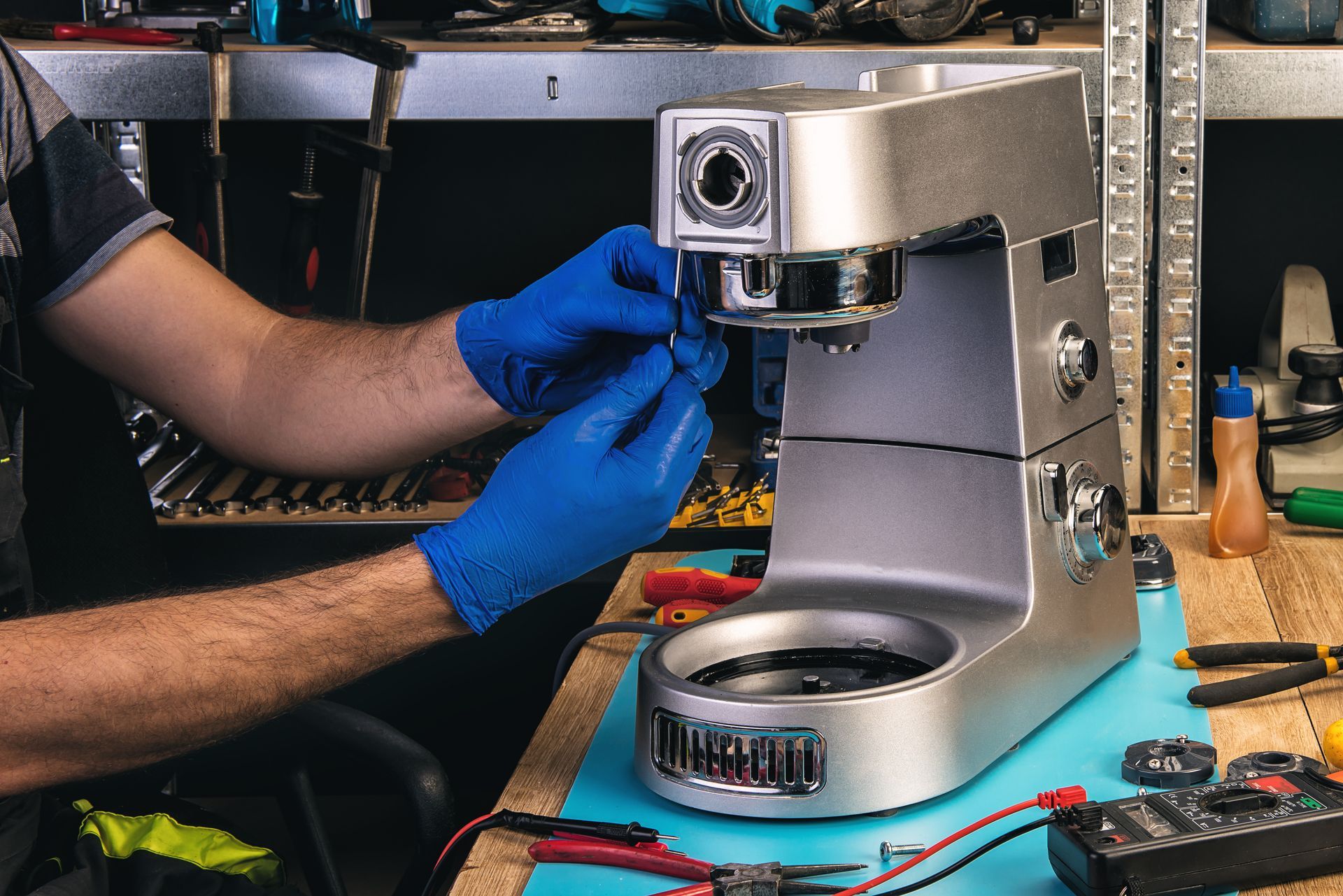 Person in blue gloves repairing a silver espresso machine on a workbench.