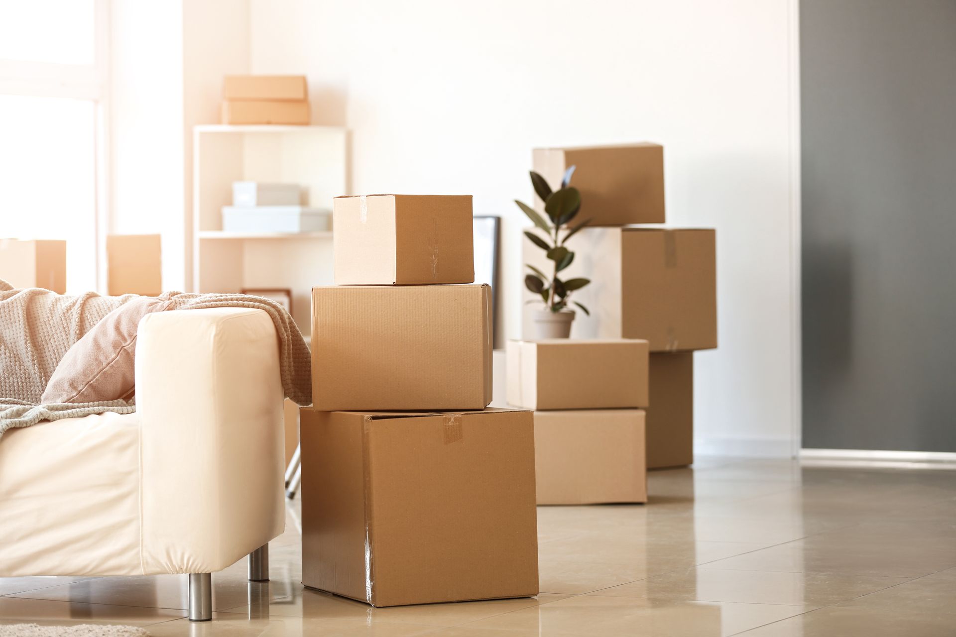 Stacked cardboard moving boxes in a bright living room beside a sofa