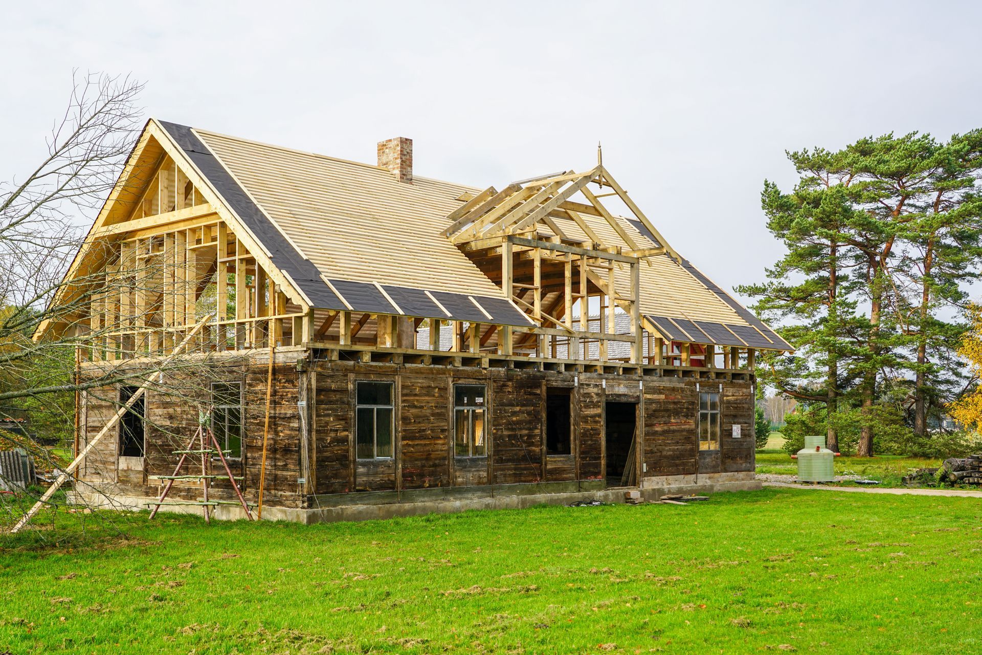 Partially built wooden house with exposed framing on a green lawn under a cloudy sky