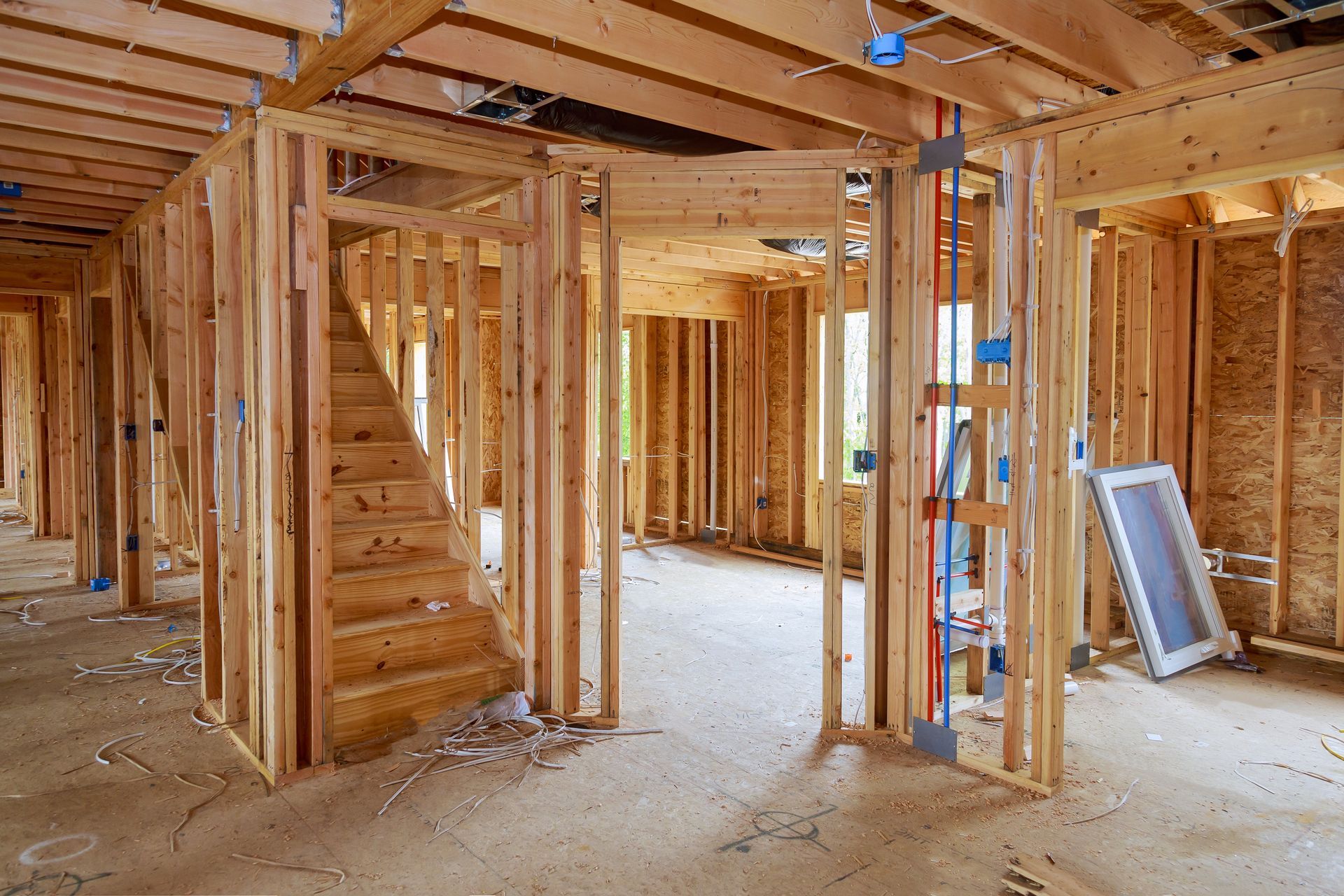 Interior of a wood-framed house under construction, with exposed beams, stairs, and unfinished walls.