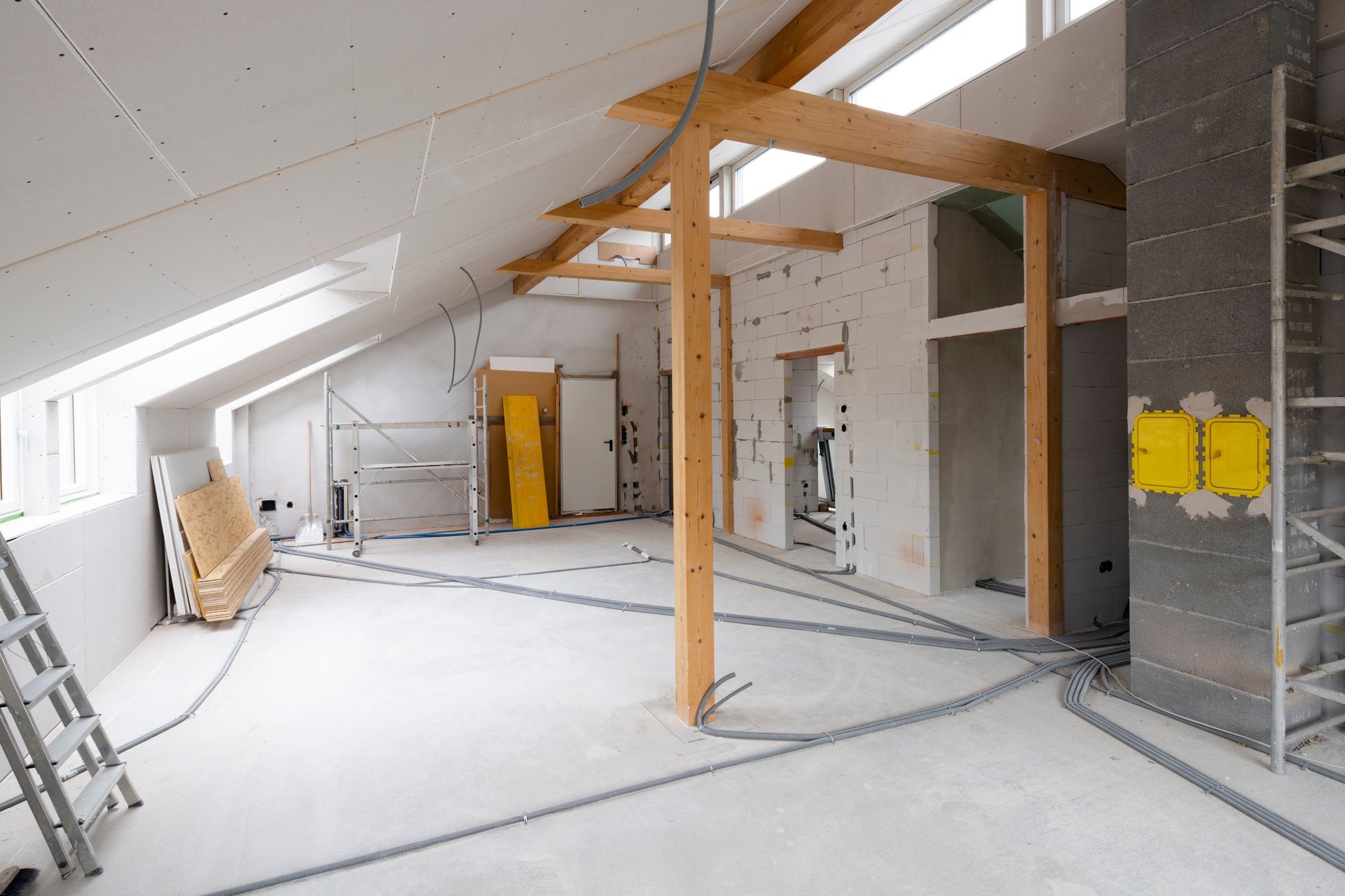 Unfinished attic room with exposed beams, white walls, and a ladder leaning on the left side.