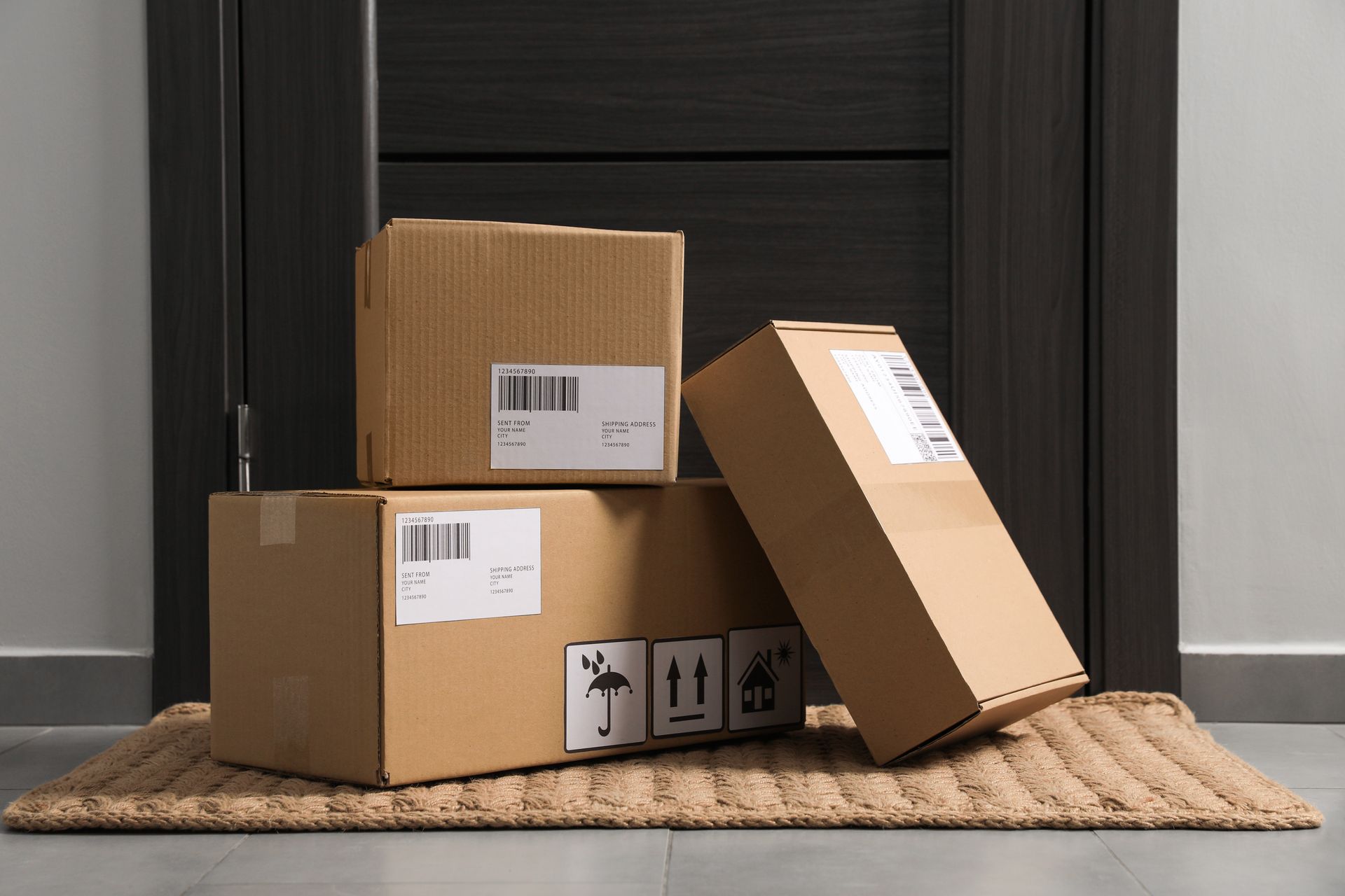 Three cardboard shipping boxes stacked on a doormat in front of a dark door