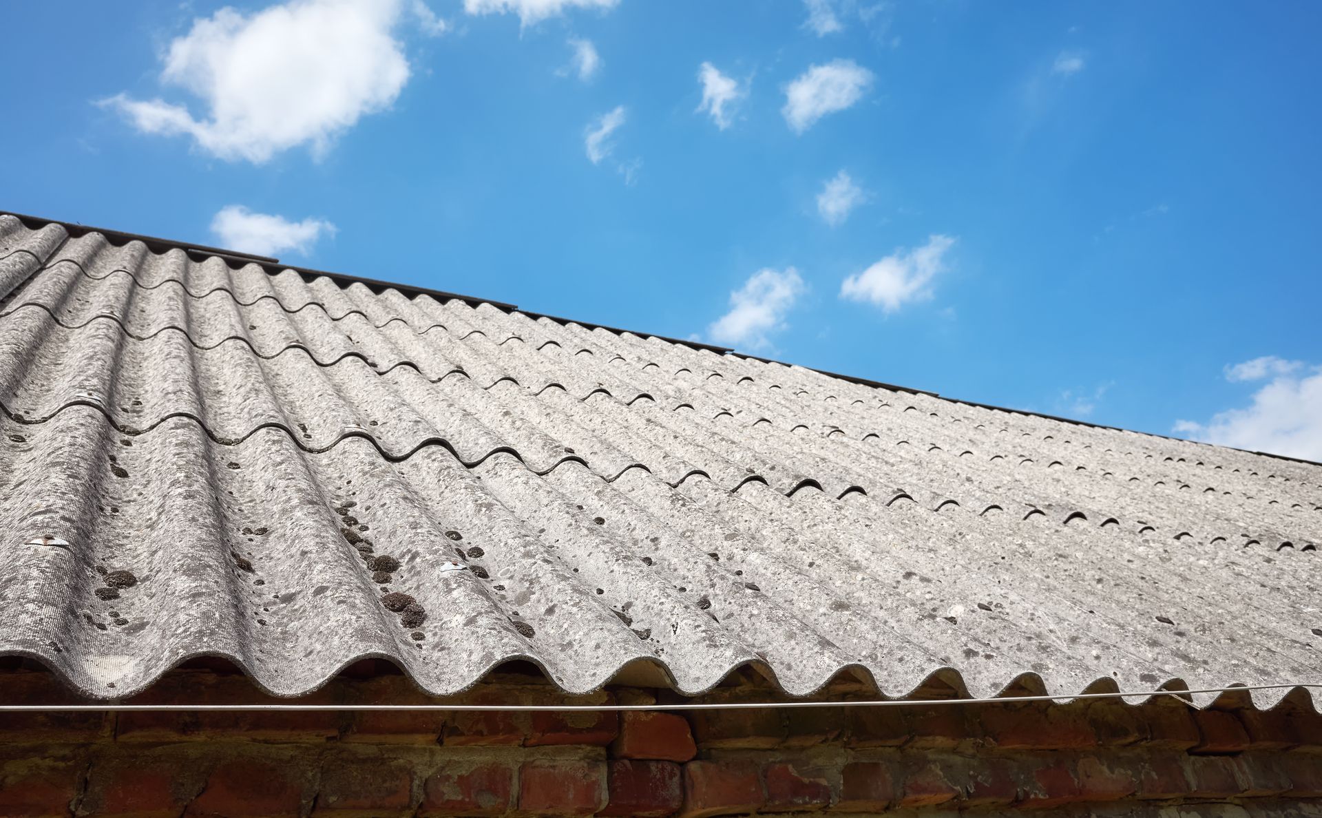 Weathered corrugated roof under a bright blue sky with scattered white clouds