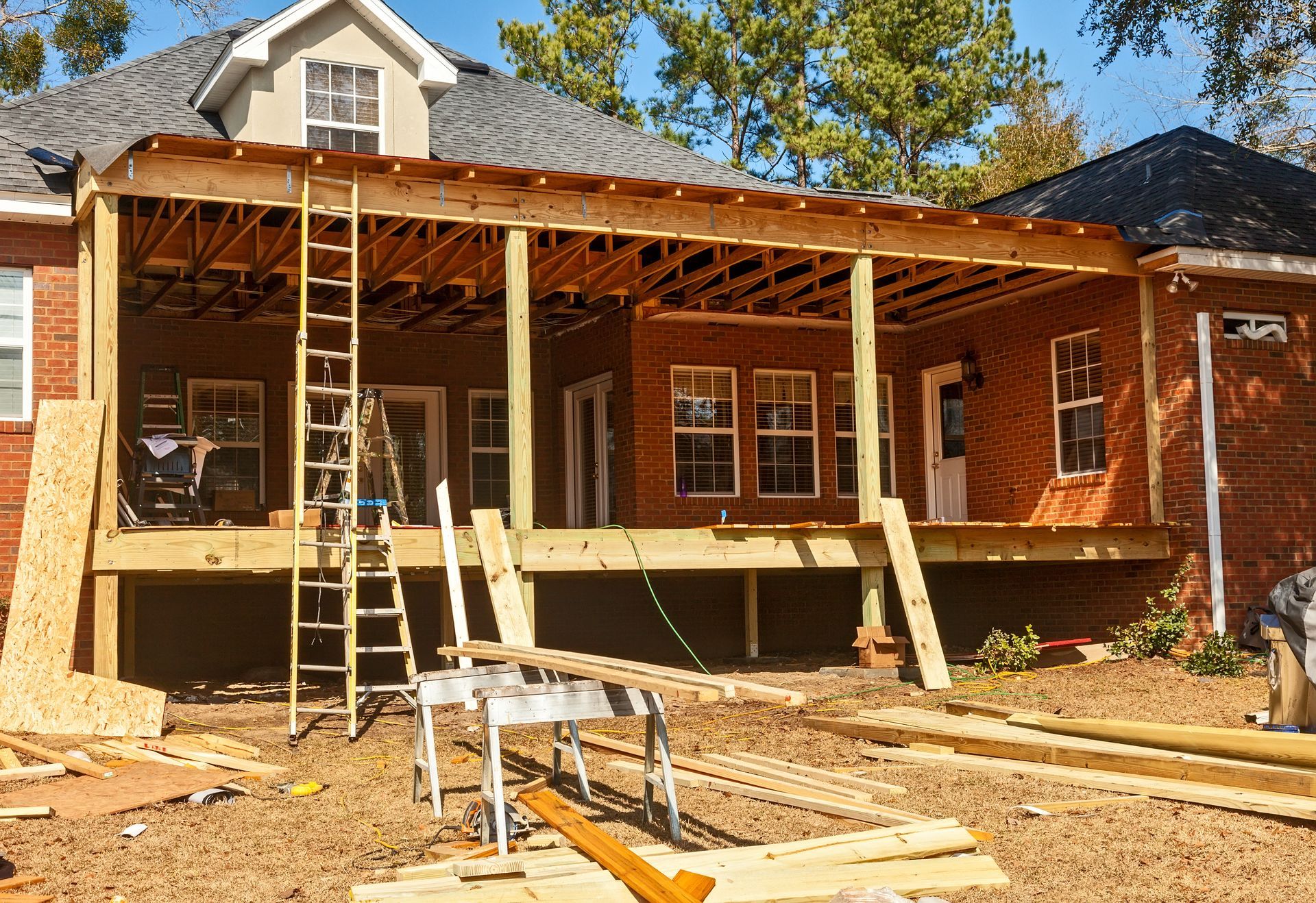 Front porch under construction on a brick house, with exposed framing, supports, ladders, and lumber.