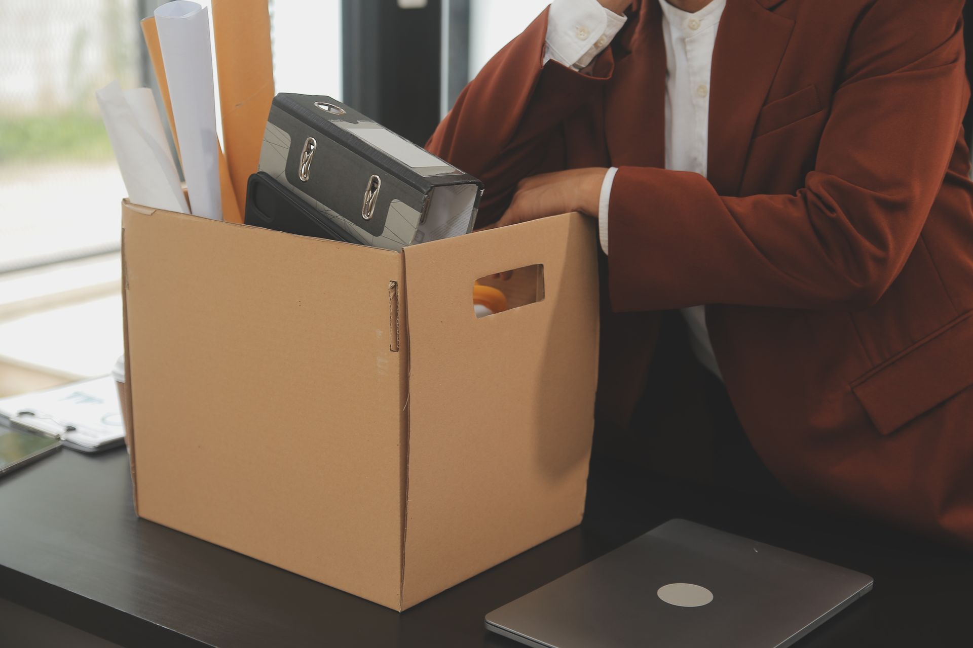 Person packing office equipment into a cardboard box on a desk