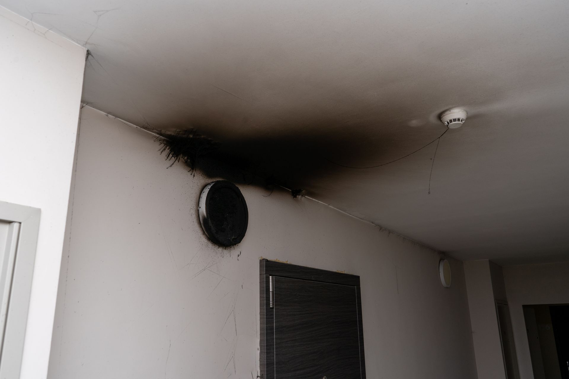 Burned ceiling and wall above a vent in a hallway, with heavy black smoke damage